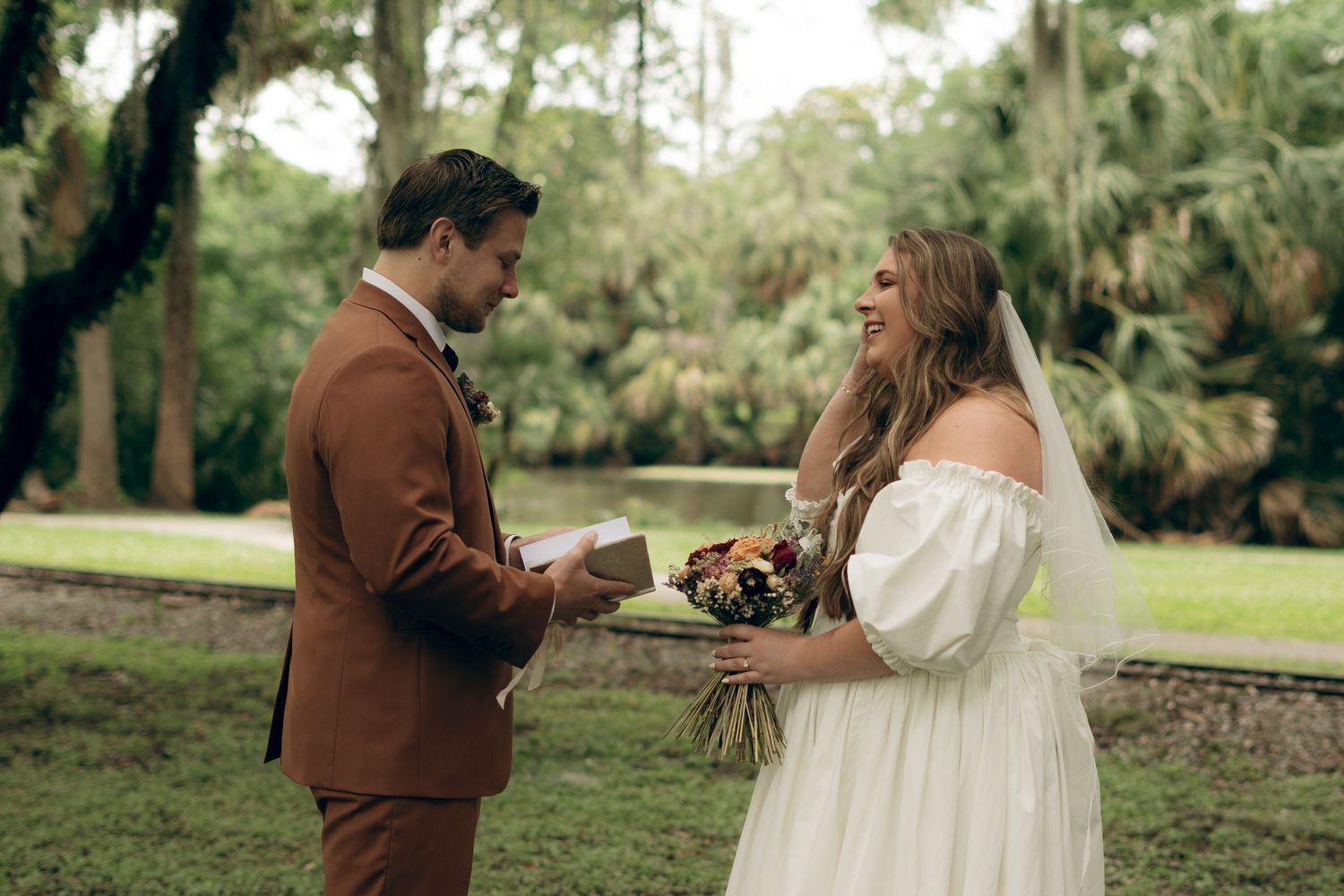 A couple exchanges rings during an intimate outdoor wedding ceremony surrounded by palm trees and lush greenery.