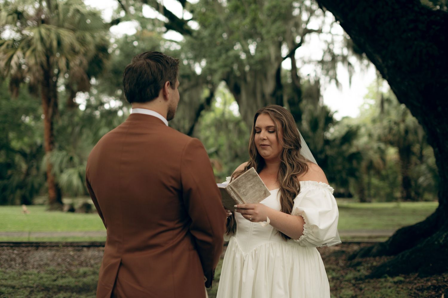 A couple exchanges vows during an intimate outdoor wedding ceremony beneath moss-draped trees.