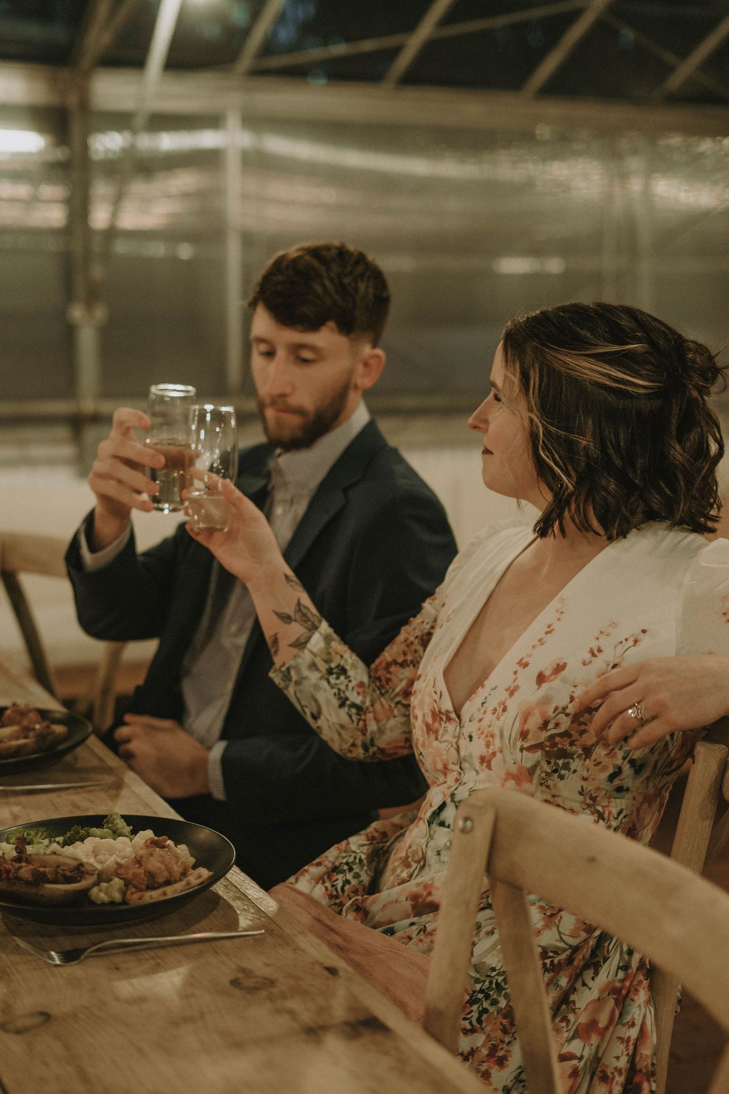 A couple toasts with wine glasses during an intimate dinner in a greenhouse setting.