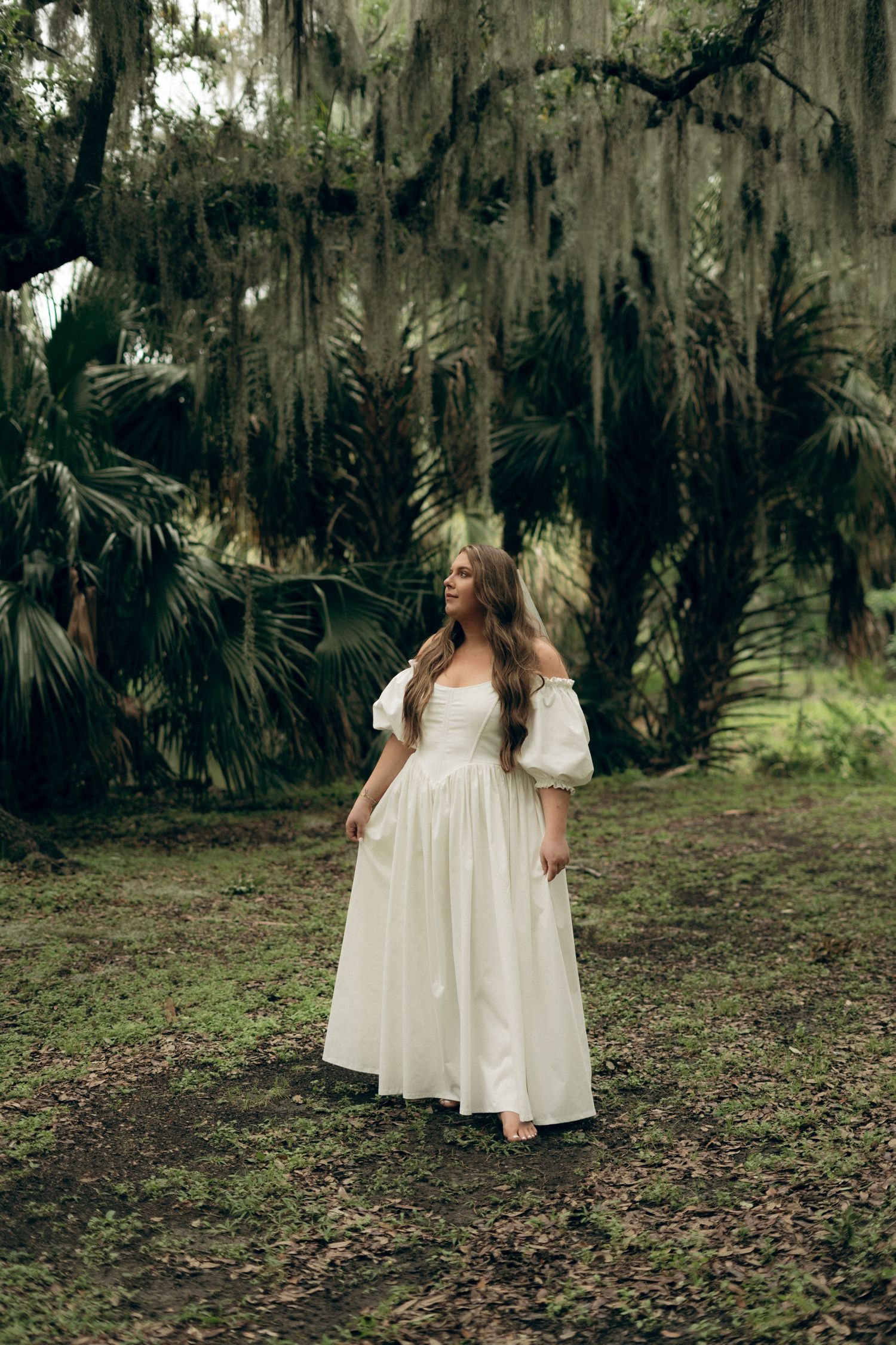 A dreamy vintage-style white dress photographed against Spanish moss and palm trees in a moody southern setting.