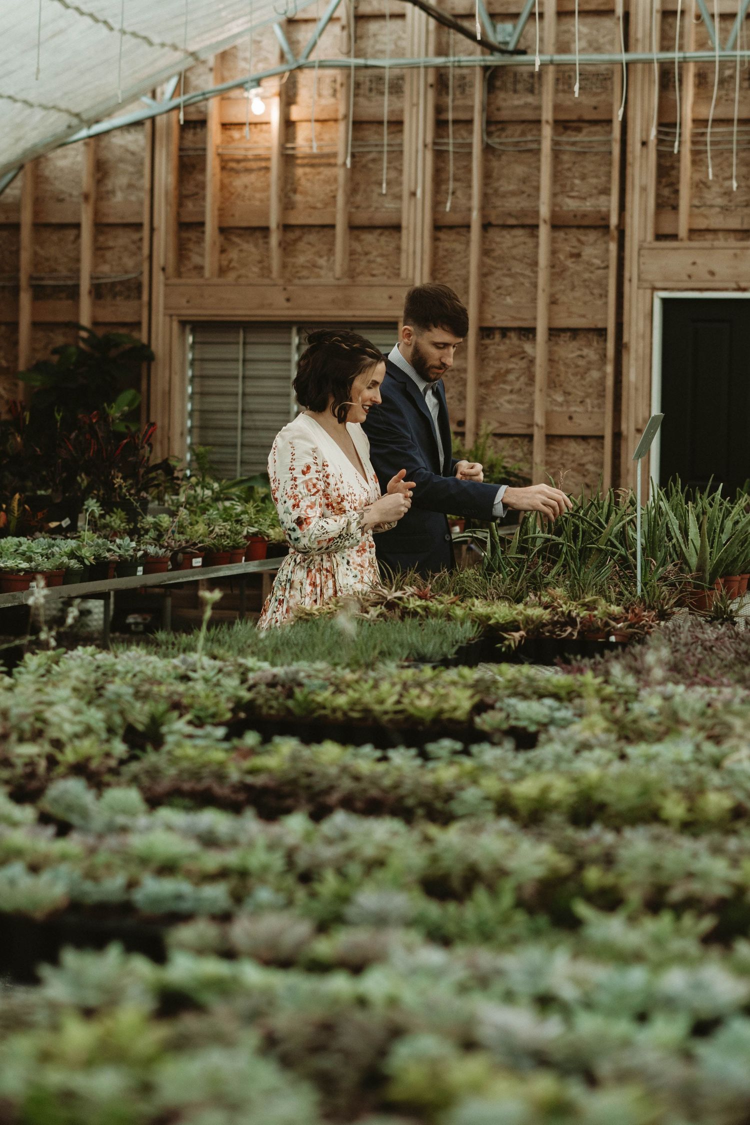 Two people examining plants together in a greenhouse with rows of greenery.