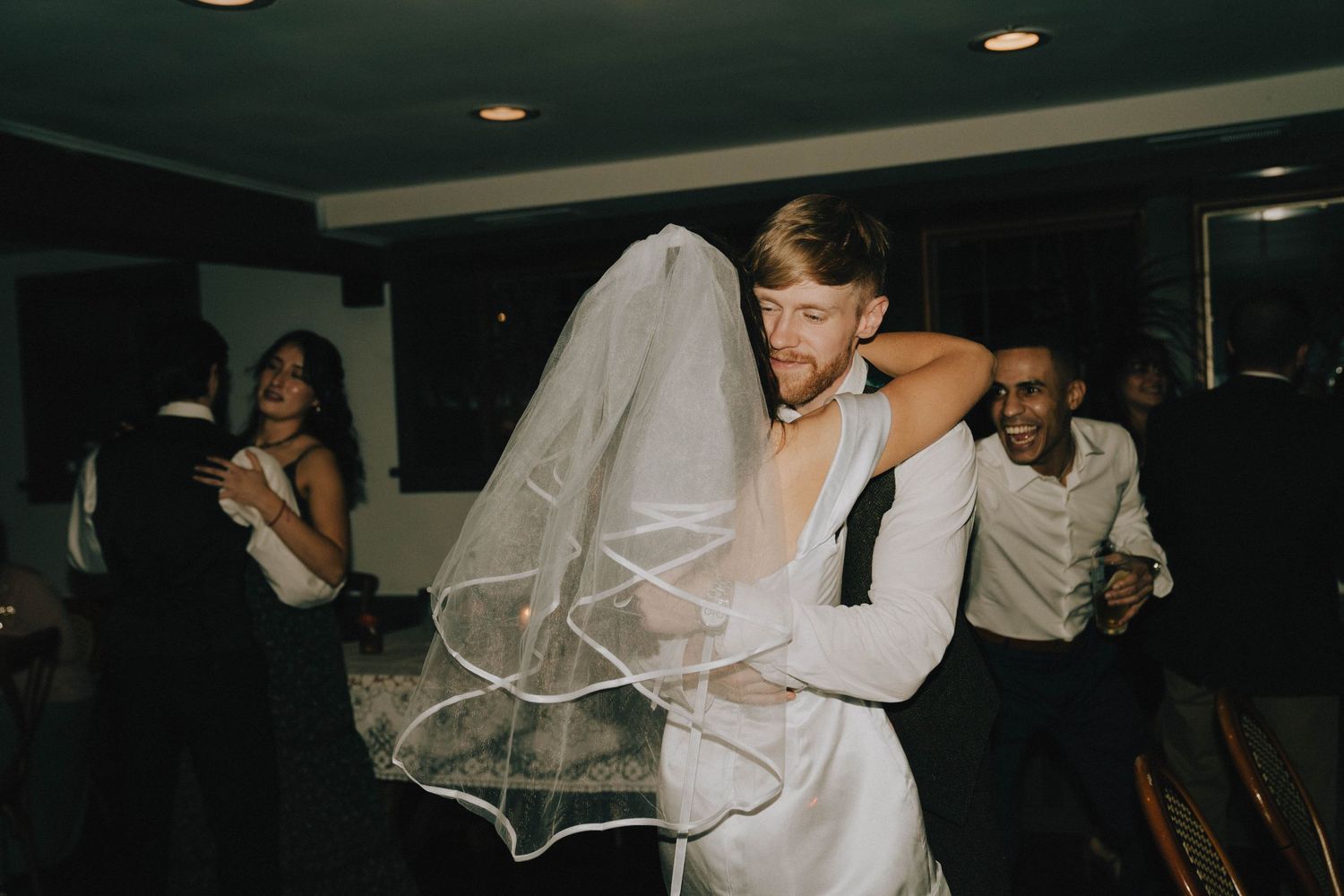 A bride and groom dance energetically at their wedding reception under dim lighting.