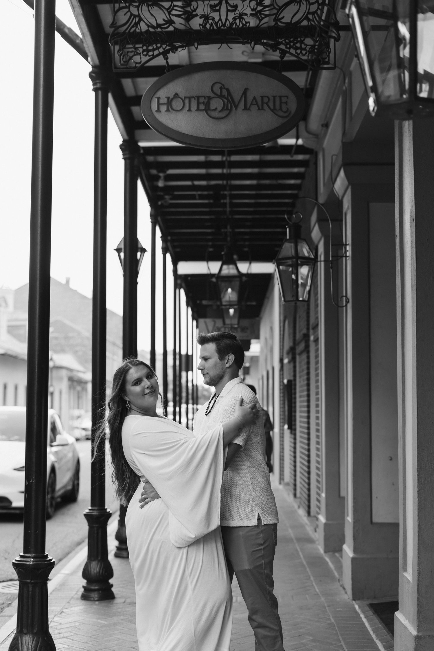 A romantic couple embraces under the ornate covered walkway of Hotel Marie in black and white.