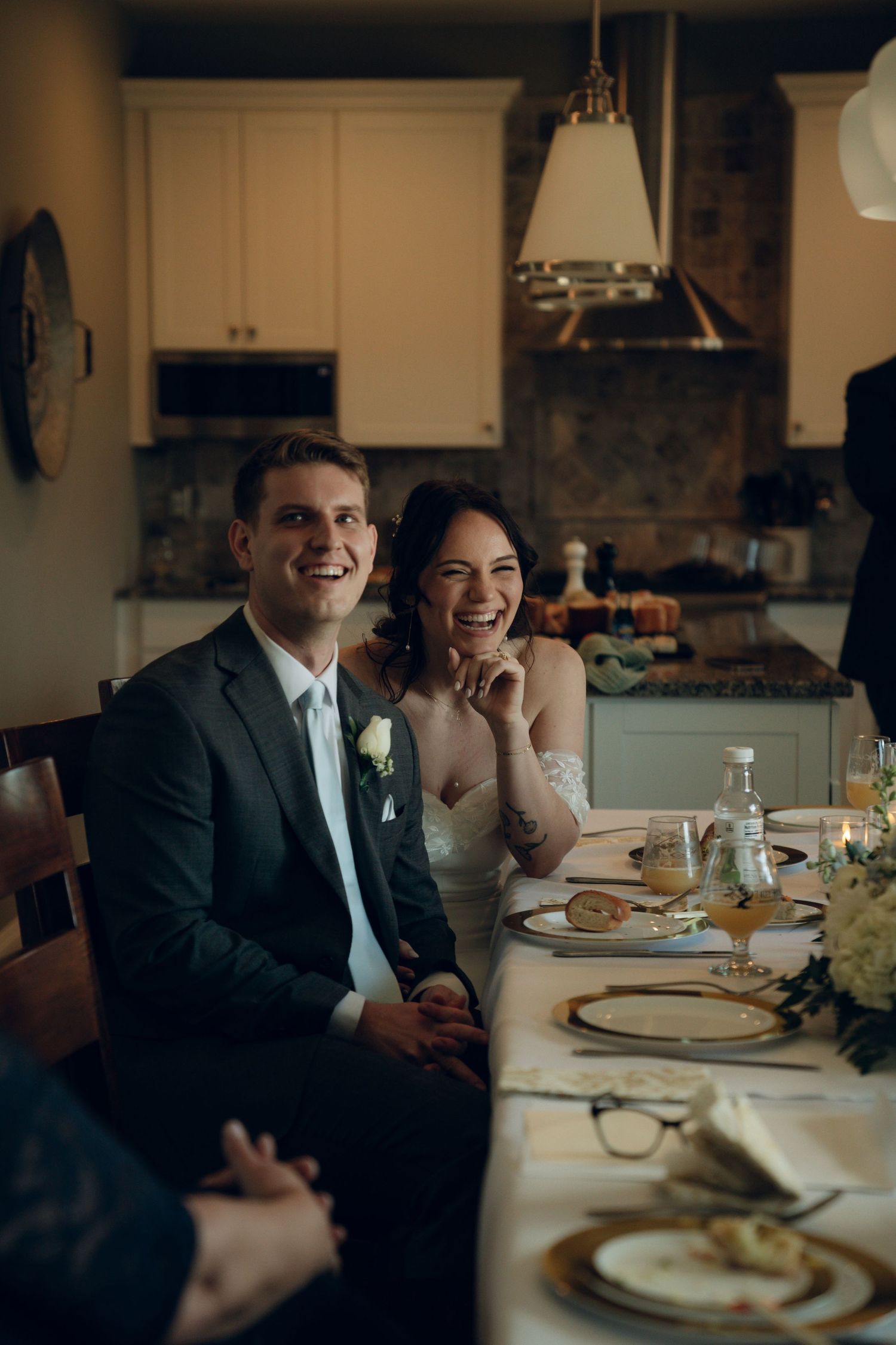 A couple in formal wedding attire share a joyful moment at an elegant dining table with place settings and decor.