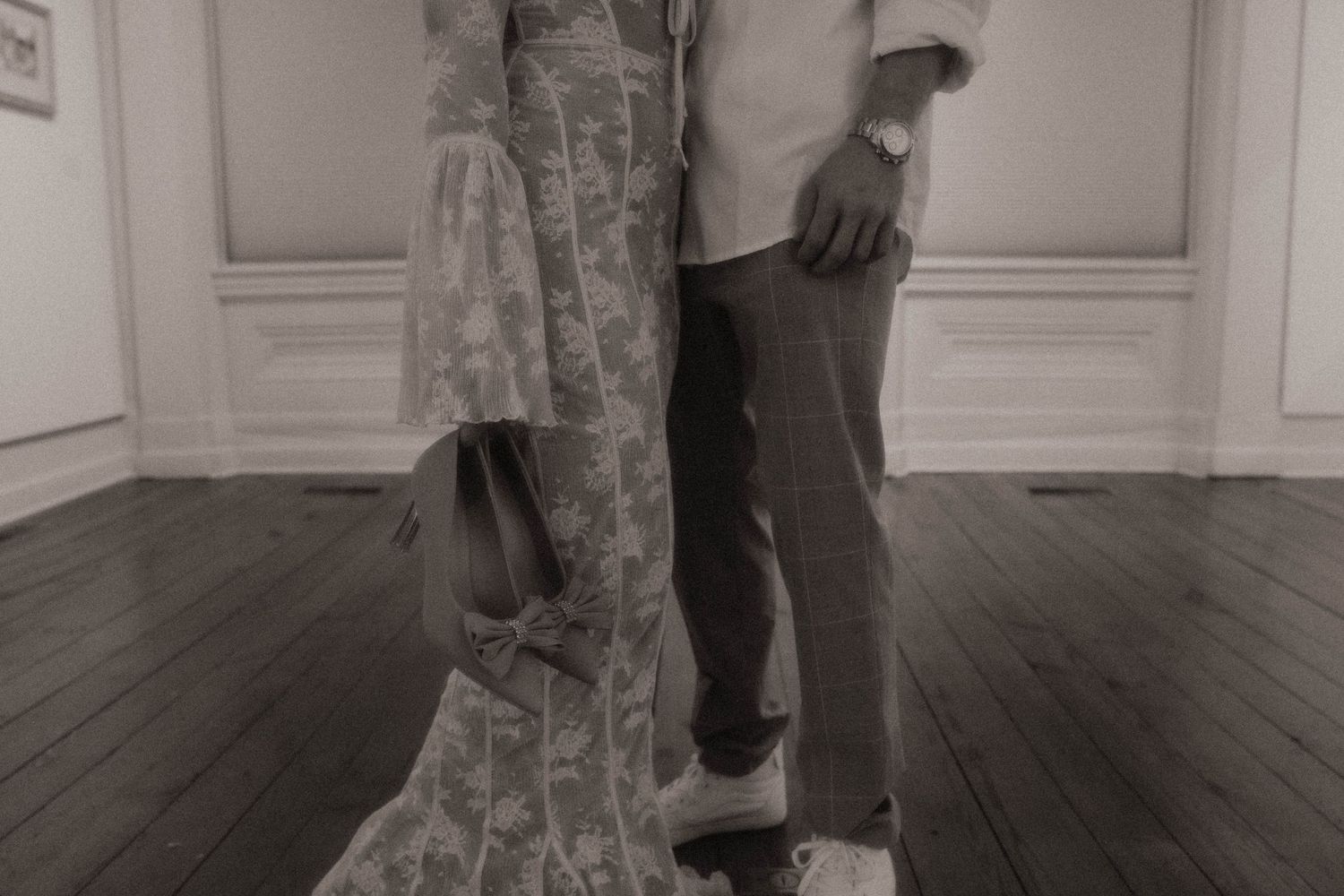 Close-up of formal dress and suit hemlines on hardwood floor in monochrome.