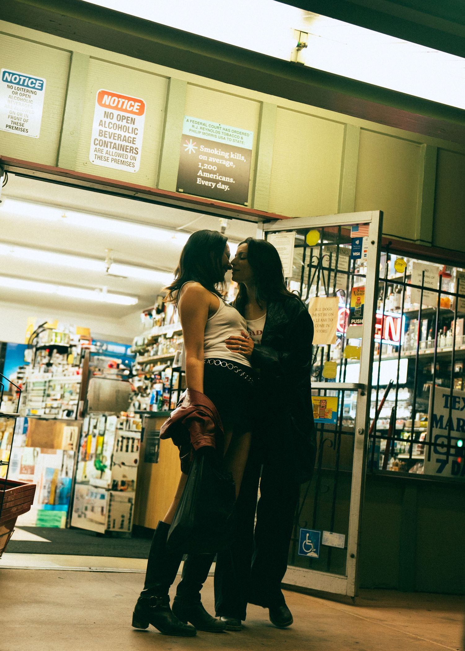 People stand in a dimly lit indoor corridor area near storefronts and notice boards at night.