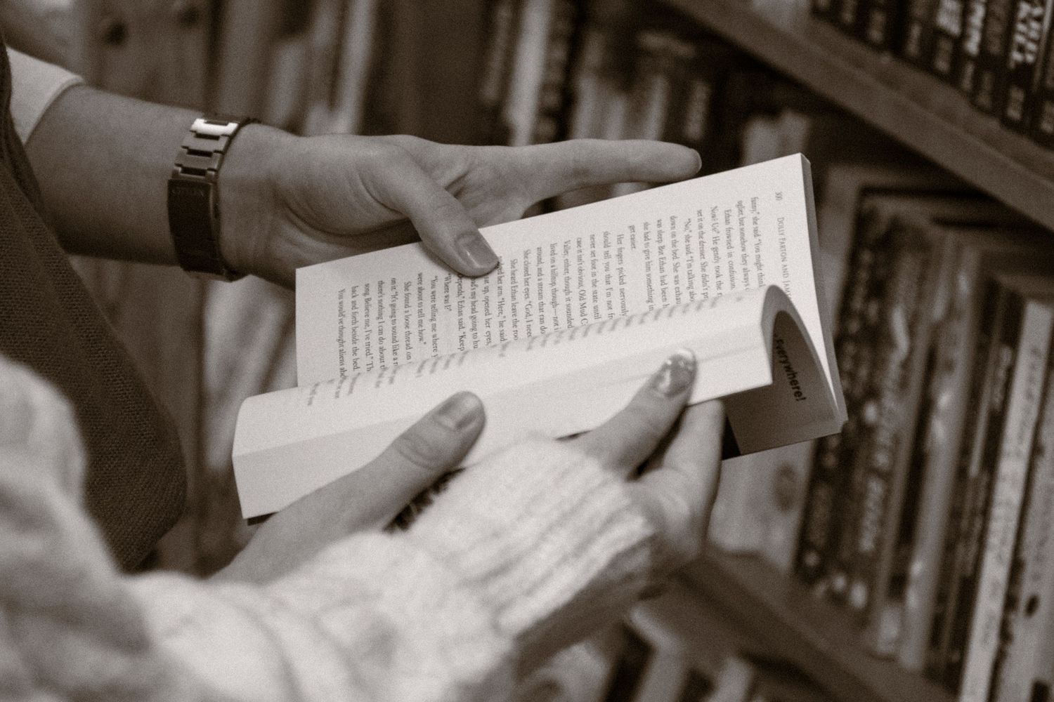 A black and white photograph shows hands holding and reading from the pages of an open book.Couple in Bar Harbor Maine