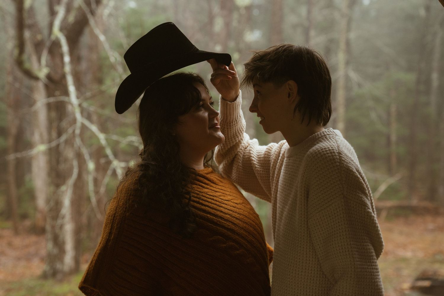 A couple in formal wedding attire embraces in a misty forest setting during an outdoor photo session.
