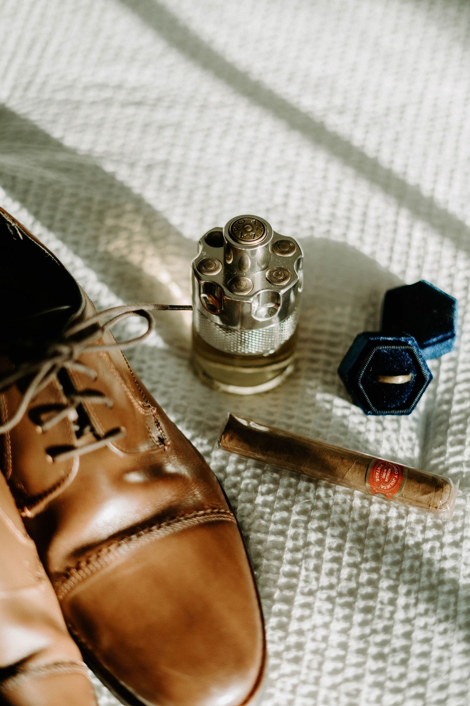 Wedding details featuring brown leather dress shoes, cufflinks and accessories on white fabric.
