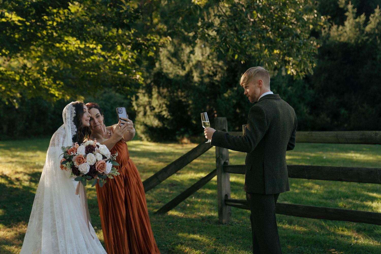 Wedding guests take photos on their phones during an outdoor ceremony.