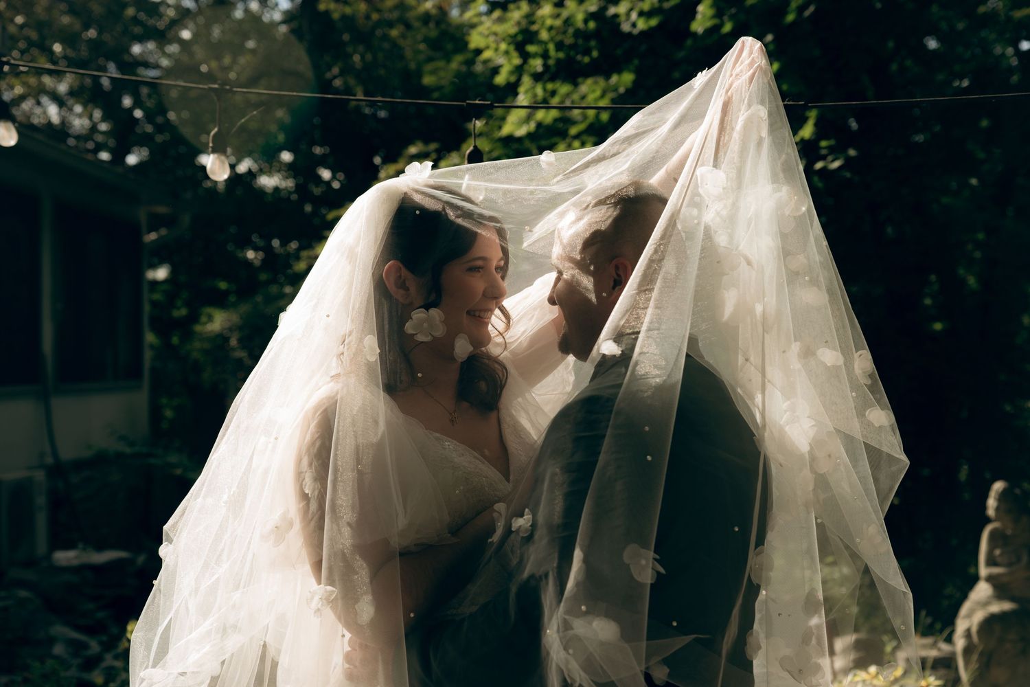 A romantic moment between newlyweds sharing a kiss under a flowing white wedding veil outdoors.