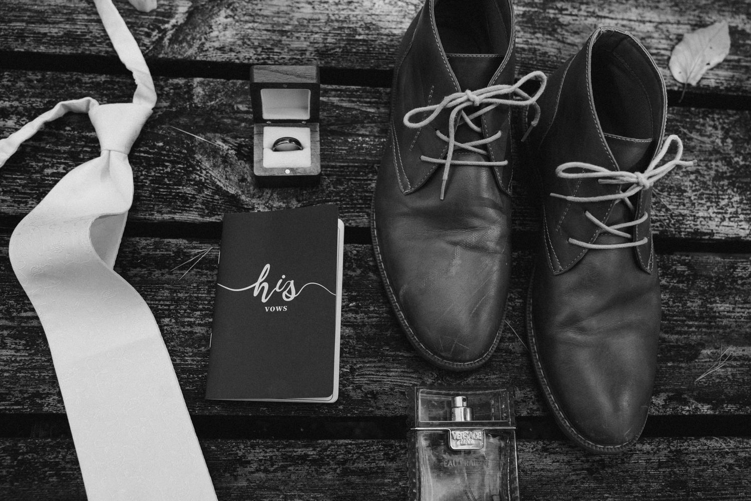 Wedding preparation details including dress, rings, notebook and formal shoes arranged on rustic wooden background.