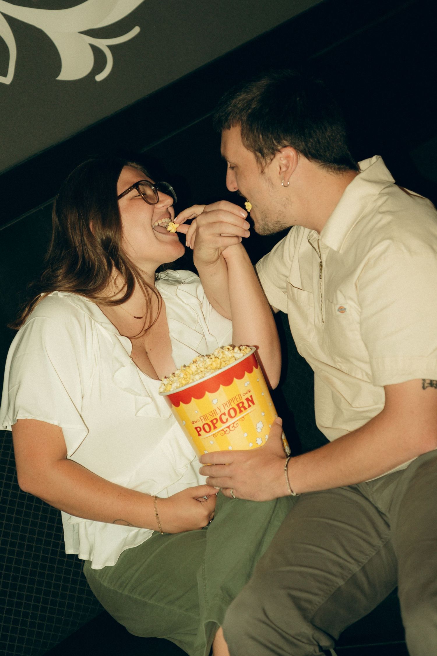 A couple sharing an intimate moment while holding a box of popcorn at the movies.