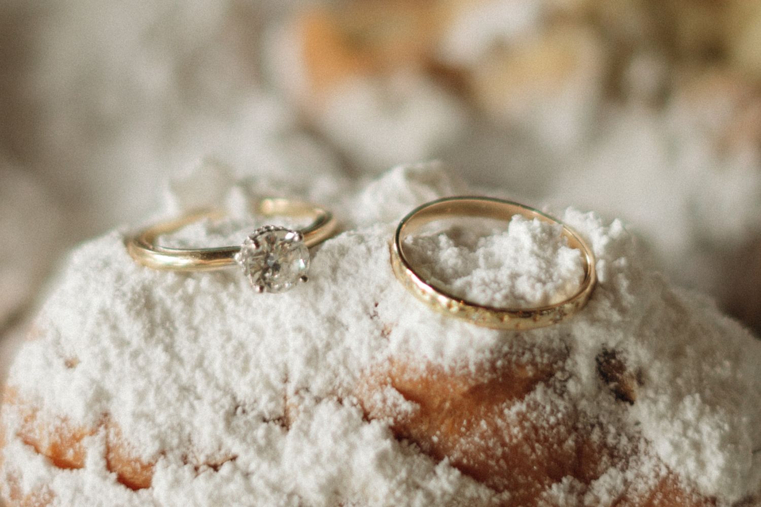 Two wedding rings resting on a white powdered surface with a soft blurred background.