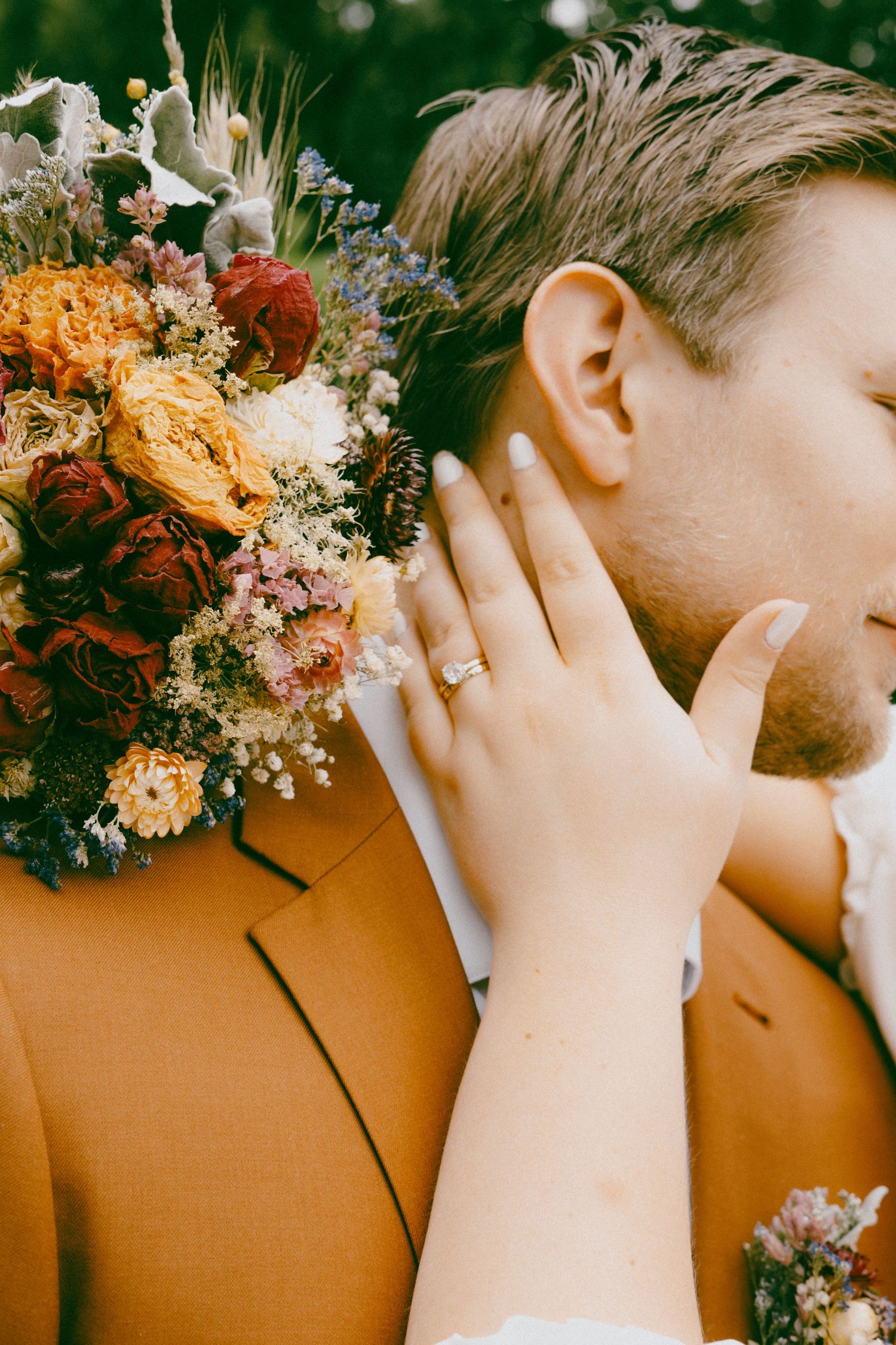 A close-up capture of two hands wearing wedding rings against a backdrop of dried flowers.