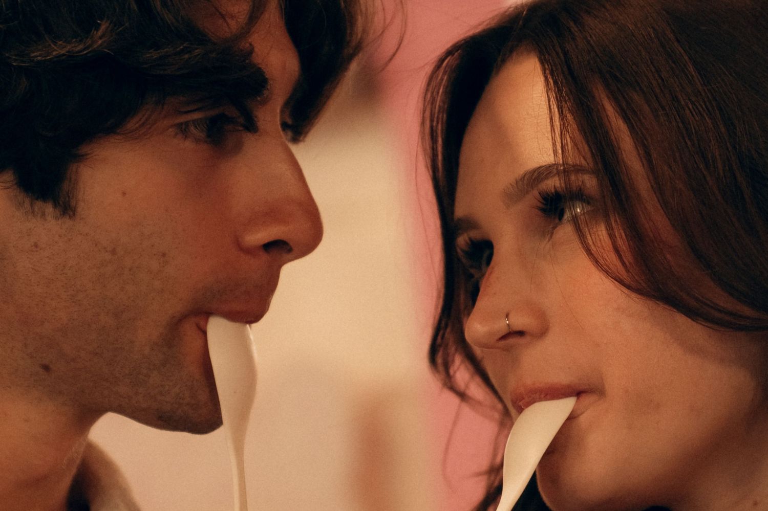 An intimate close-up photo of two people's faces leaning in close to each other in warm lighting.