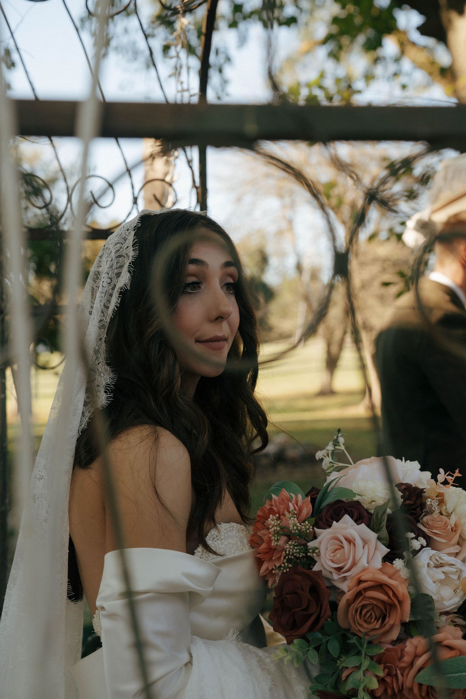 A bride in a white gown holds a romantic bouquet of roses in warm autumn light.