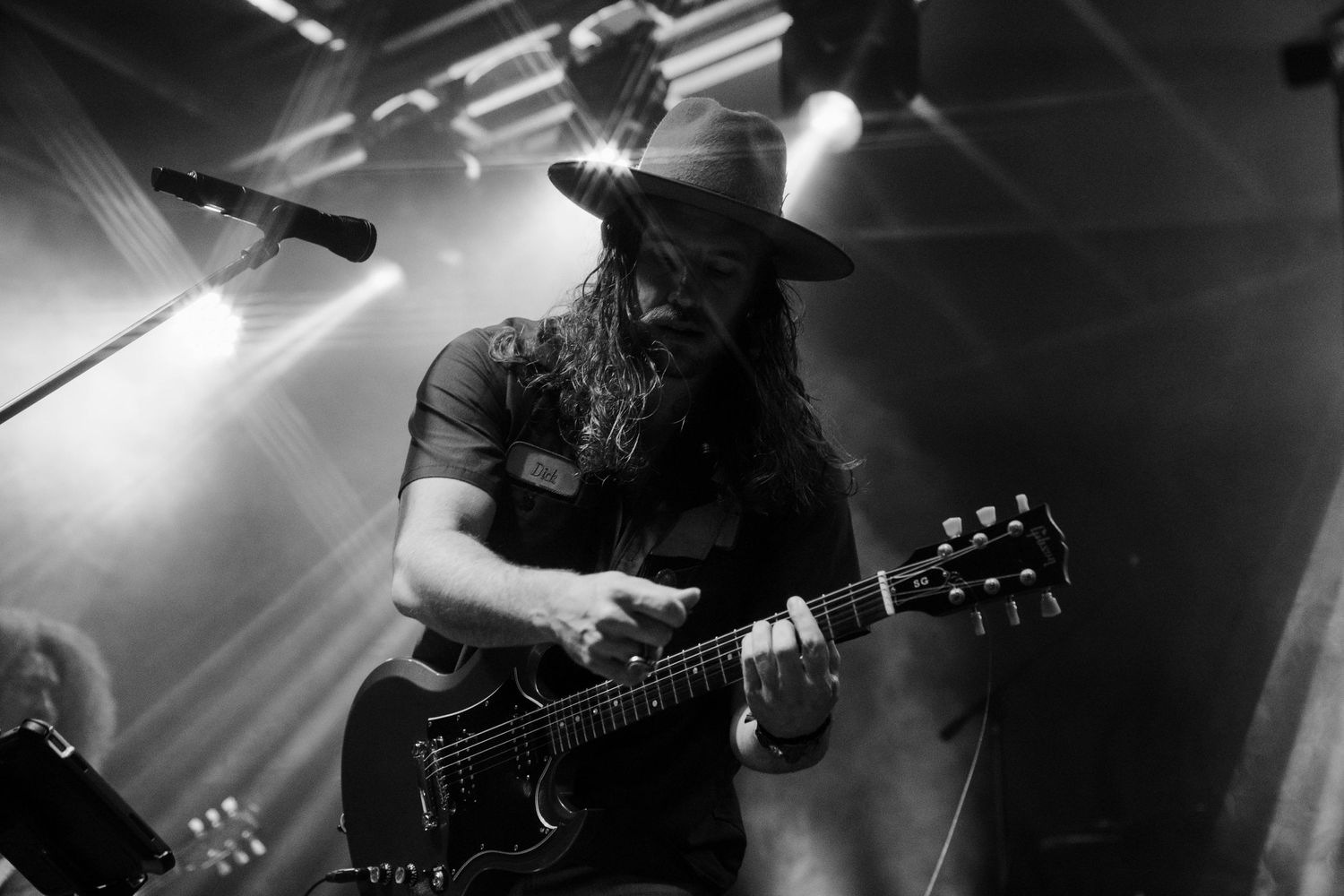 Black and white photo of a guitarist in a hat performing under stage lights.