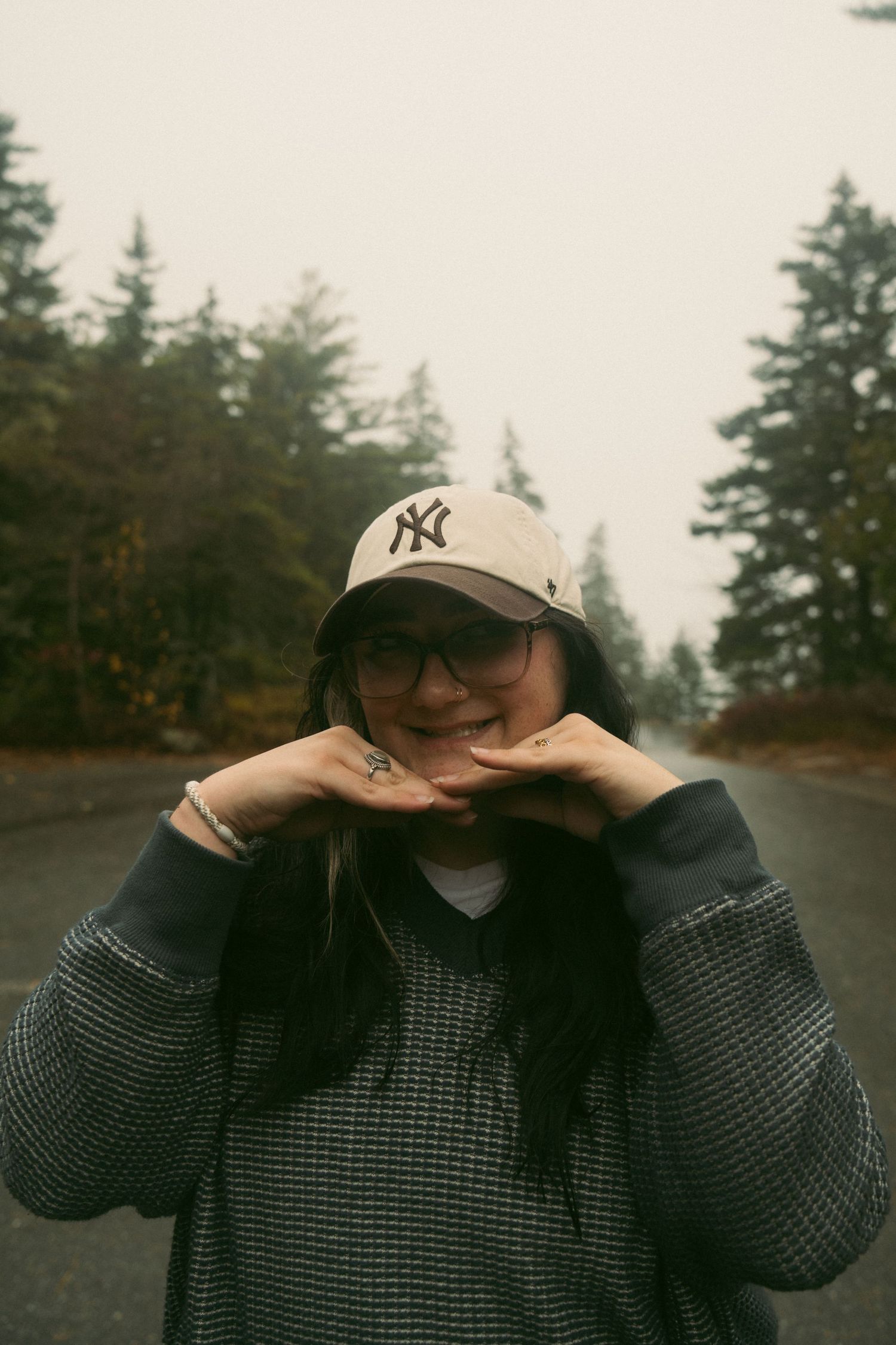 A person in a gray sweater and Yankees cap covers their face with their hands in a series of moody outdoor photos. Acadia National Park