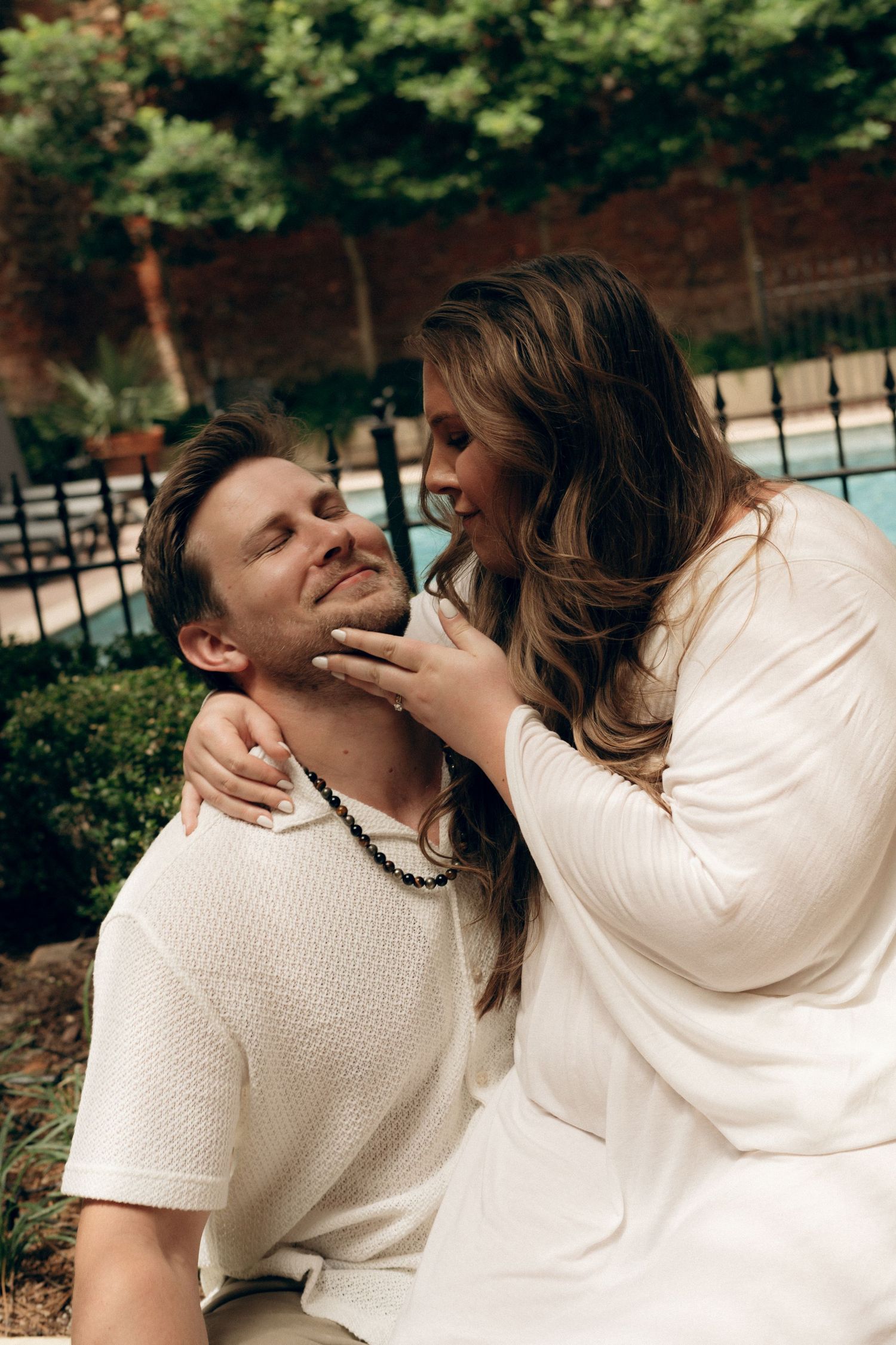 A romantic moment captured outdoors with a couple in white outfits sharing an intimate embrace.