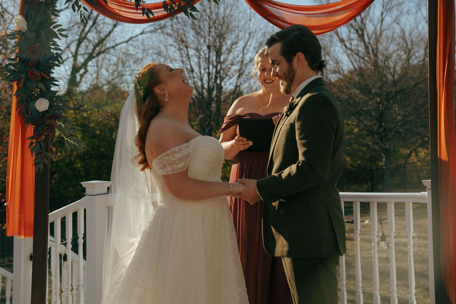 An intimate wedding ceremony on a deck with orange draping and natural autumn backdrop.