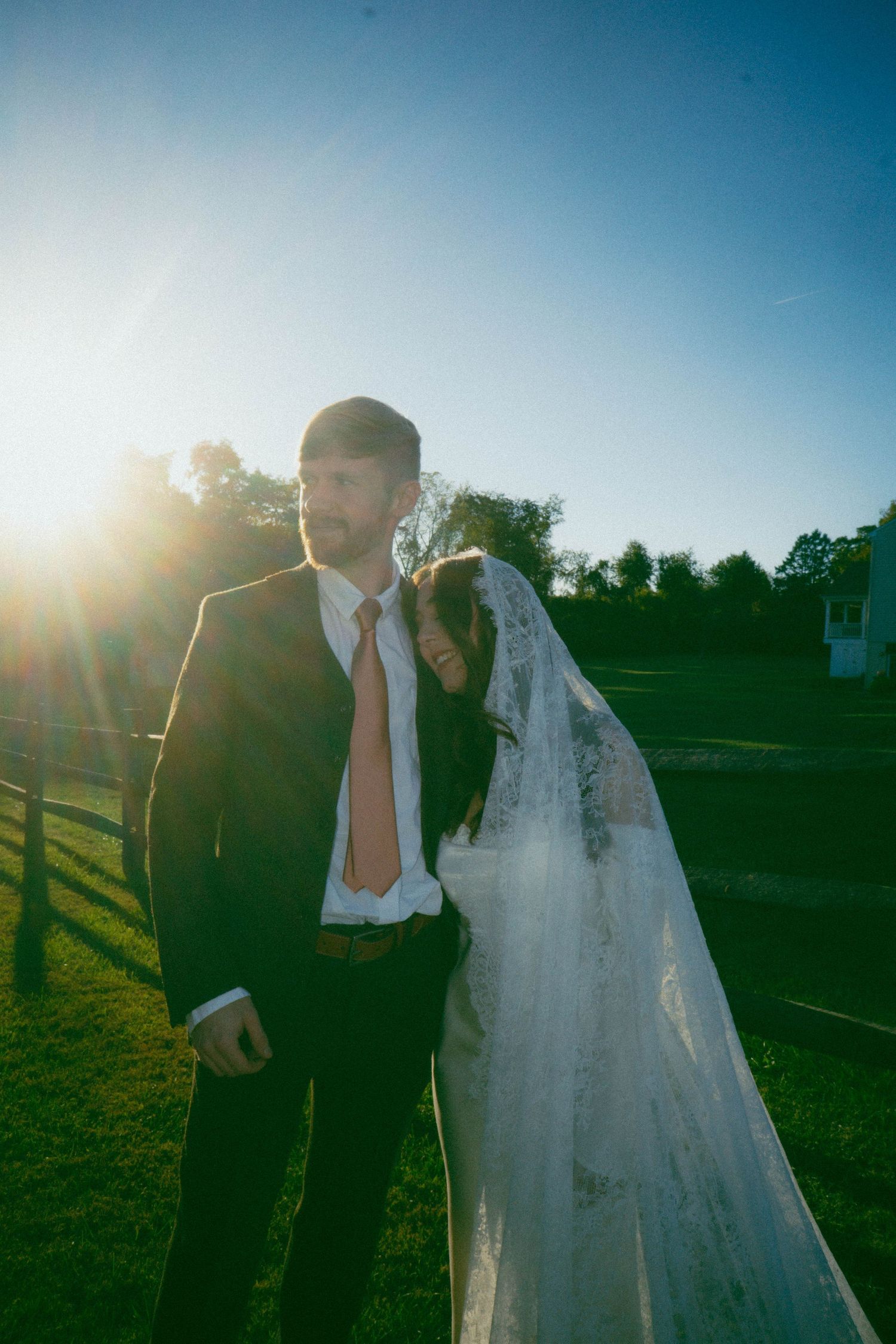 A wedding couple poses in golden sunlight against a natural outdoor backdrop.