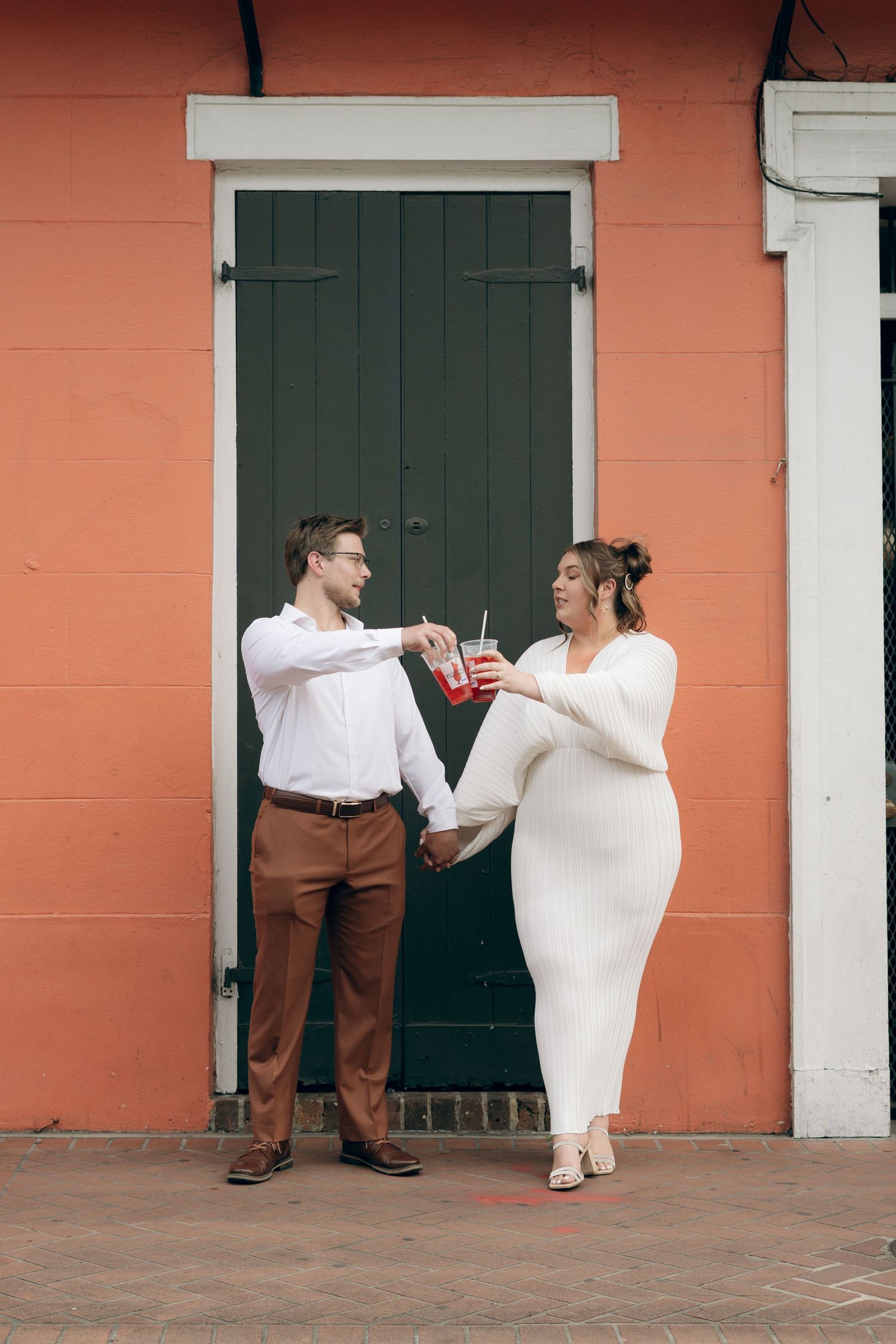 Three connected images of a bride and groom in classic wedding attire posing against a coral-colored wall with green doors.