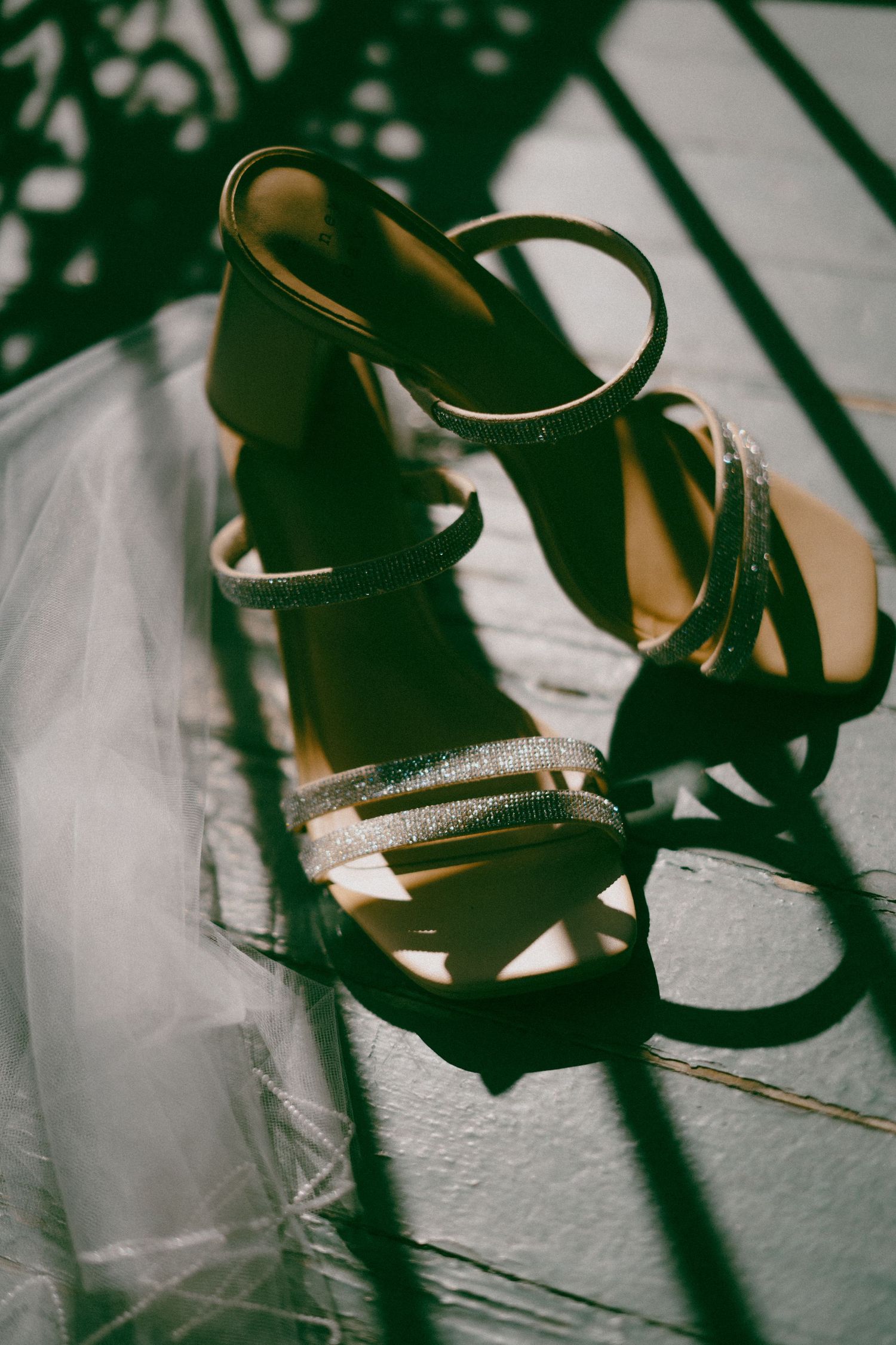 Black strappy stiletto sandals with sparkling rhinestone details cast dramatic shadows on a white surface.