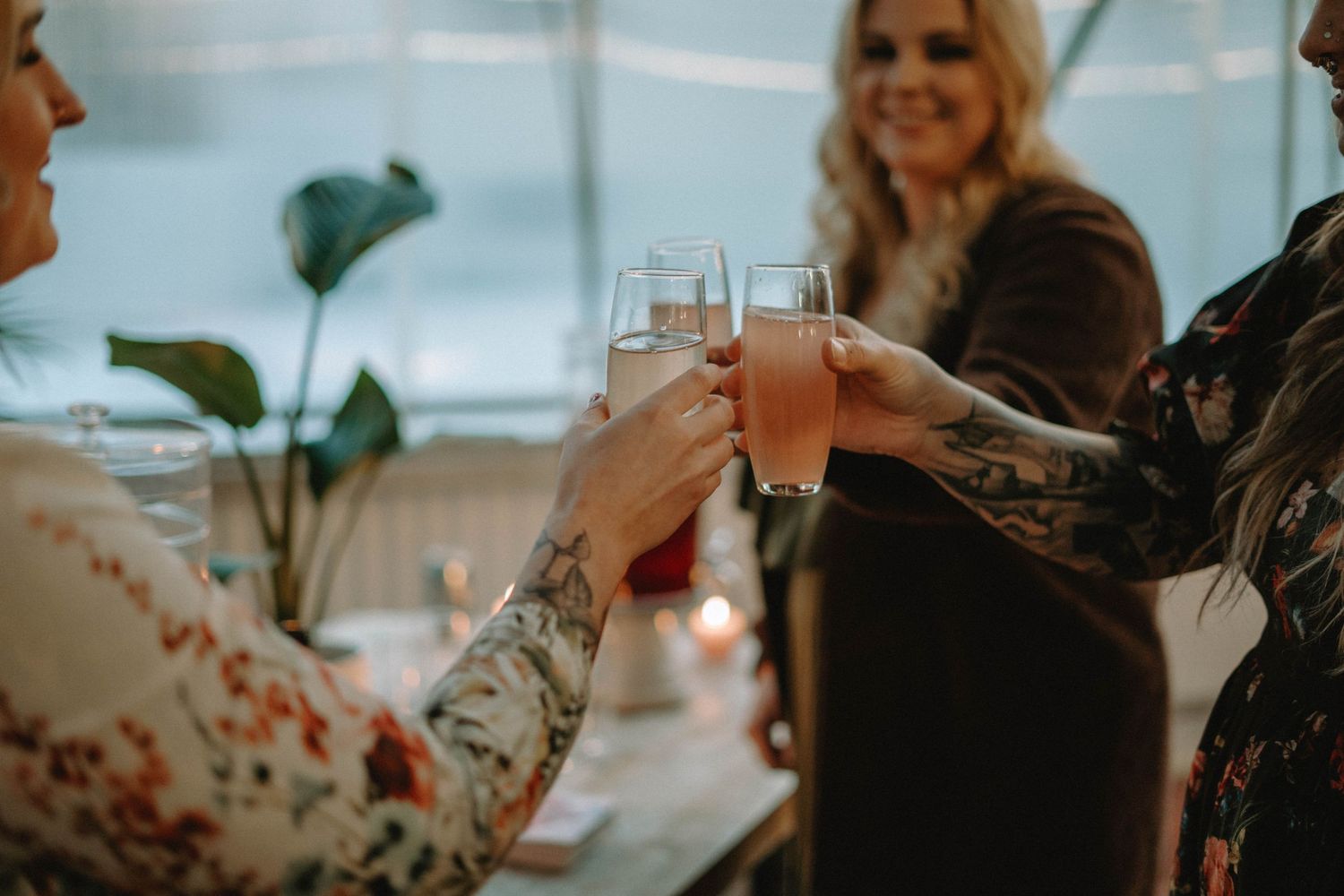 Friends toasting with cocktails at a celebration in a greenhouse setting with natural lighting.