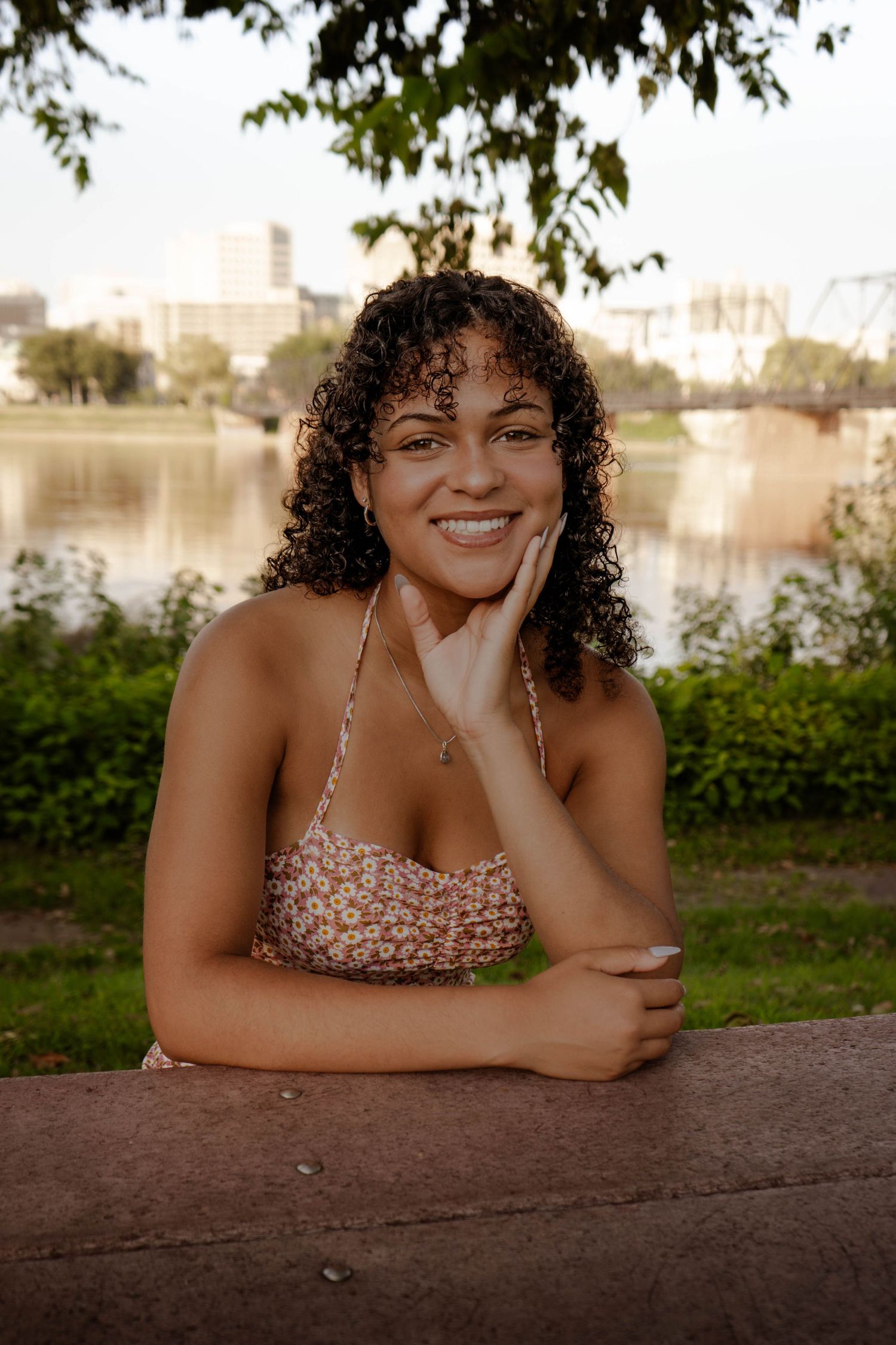 Portrait by lake with city skyline in background during golden hour.