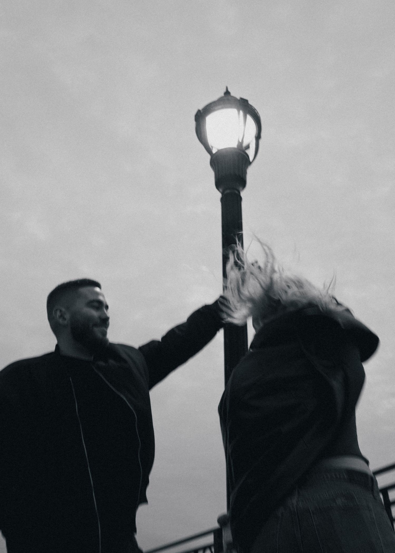 A dramatic black and white photo of two people posing by an illuminated street lamp at night. Couple in Bar Harbor Maine