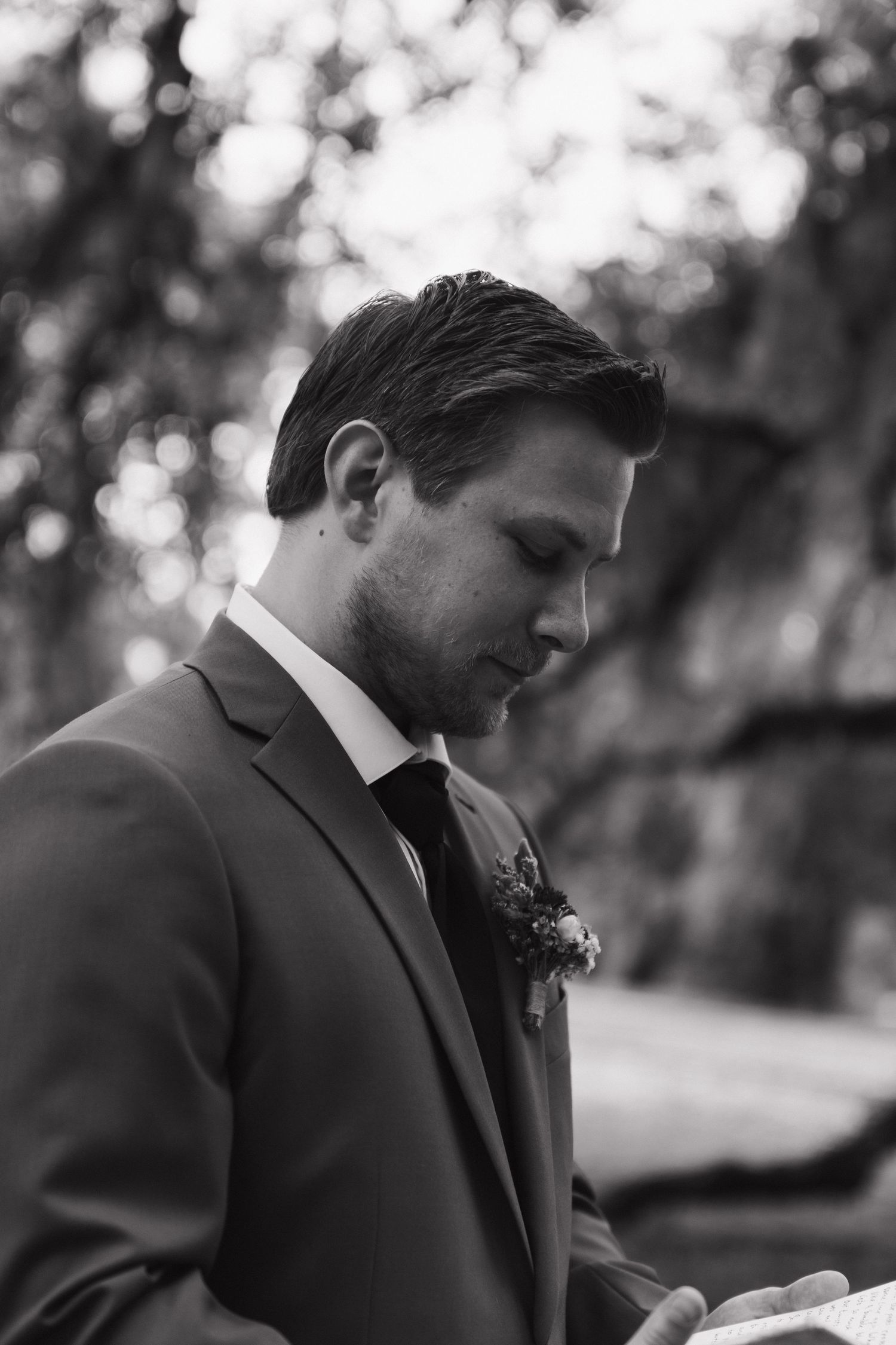 Black and white portrait of a groom in a suit with boutonniere looking contemplatively downward.