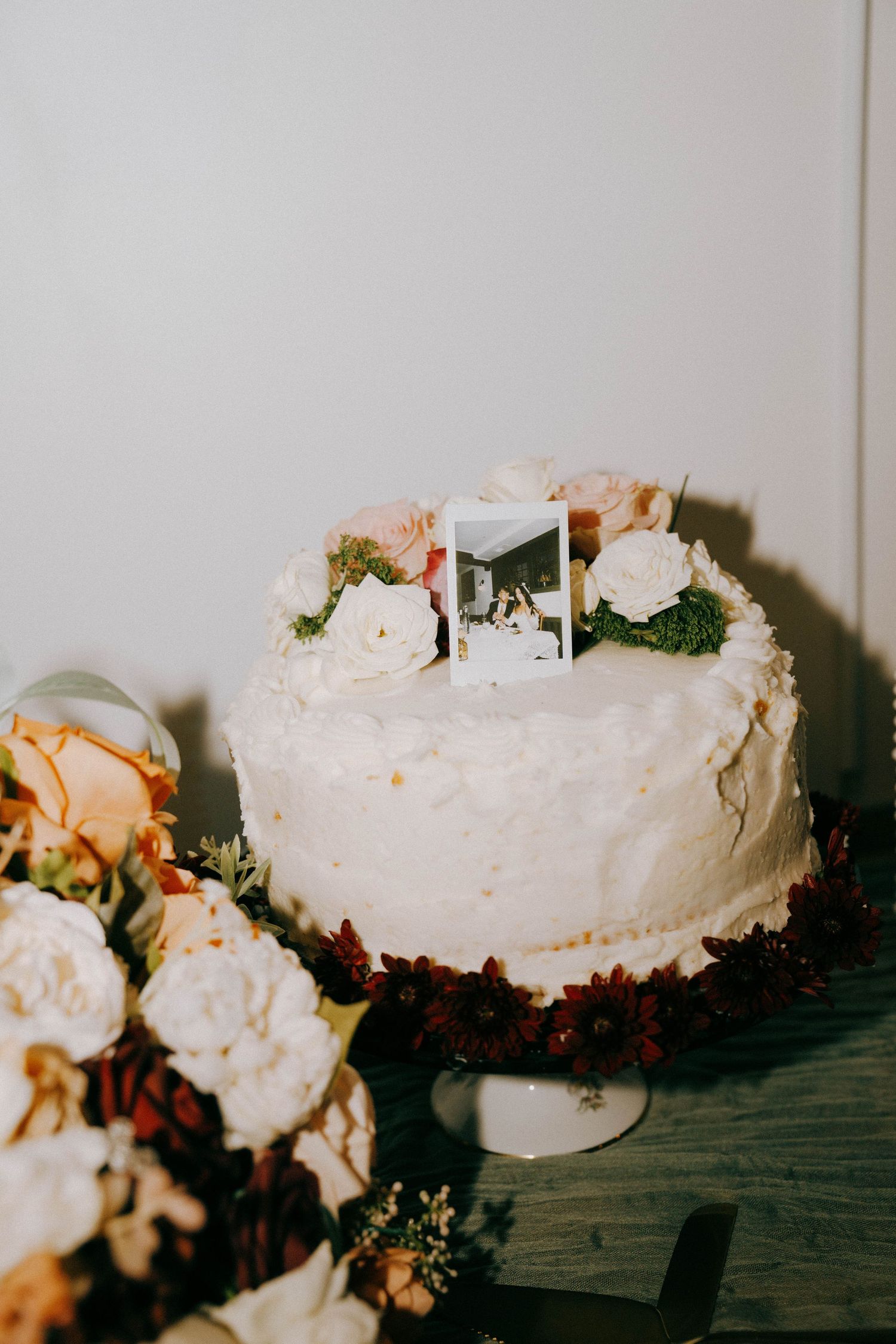 White wedding cake decorated with flowers and topped with polaroid photos.