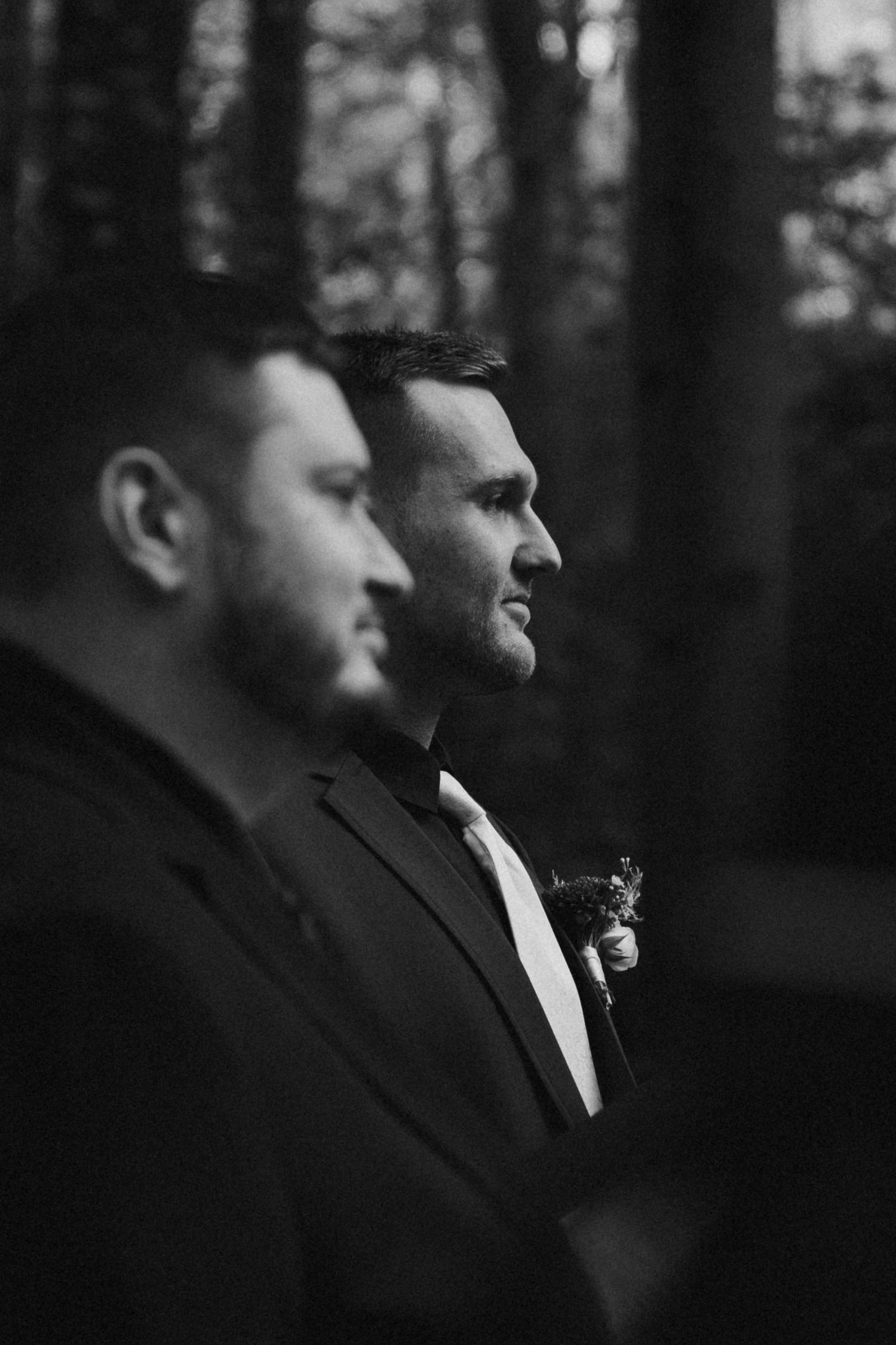 Black and white profile shot of two groomsmen at outdoor wedding.