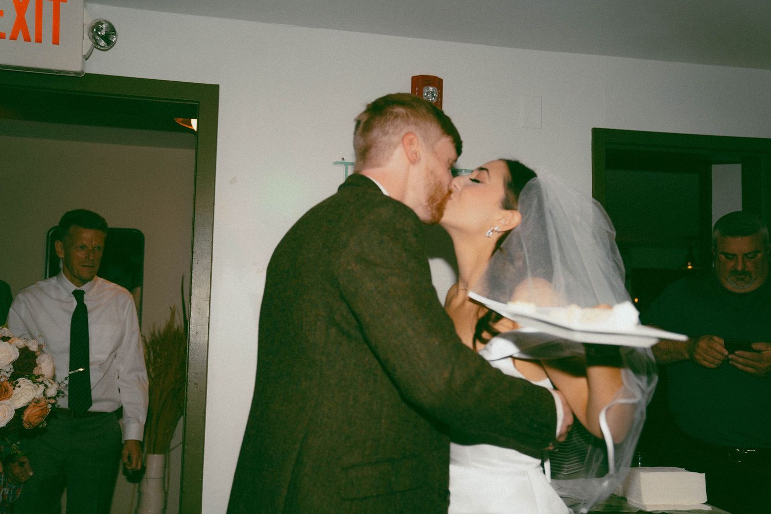 A newlywed couple shares their first bite of wedding cake together at their reception in an intimate indoor setting.