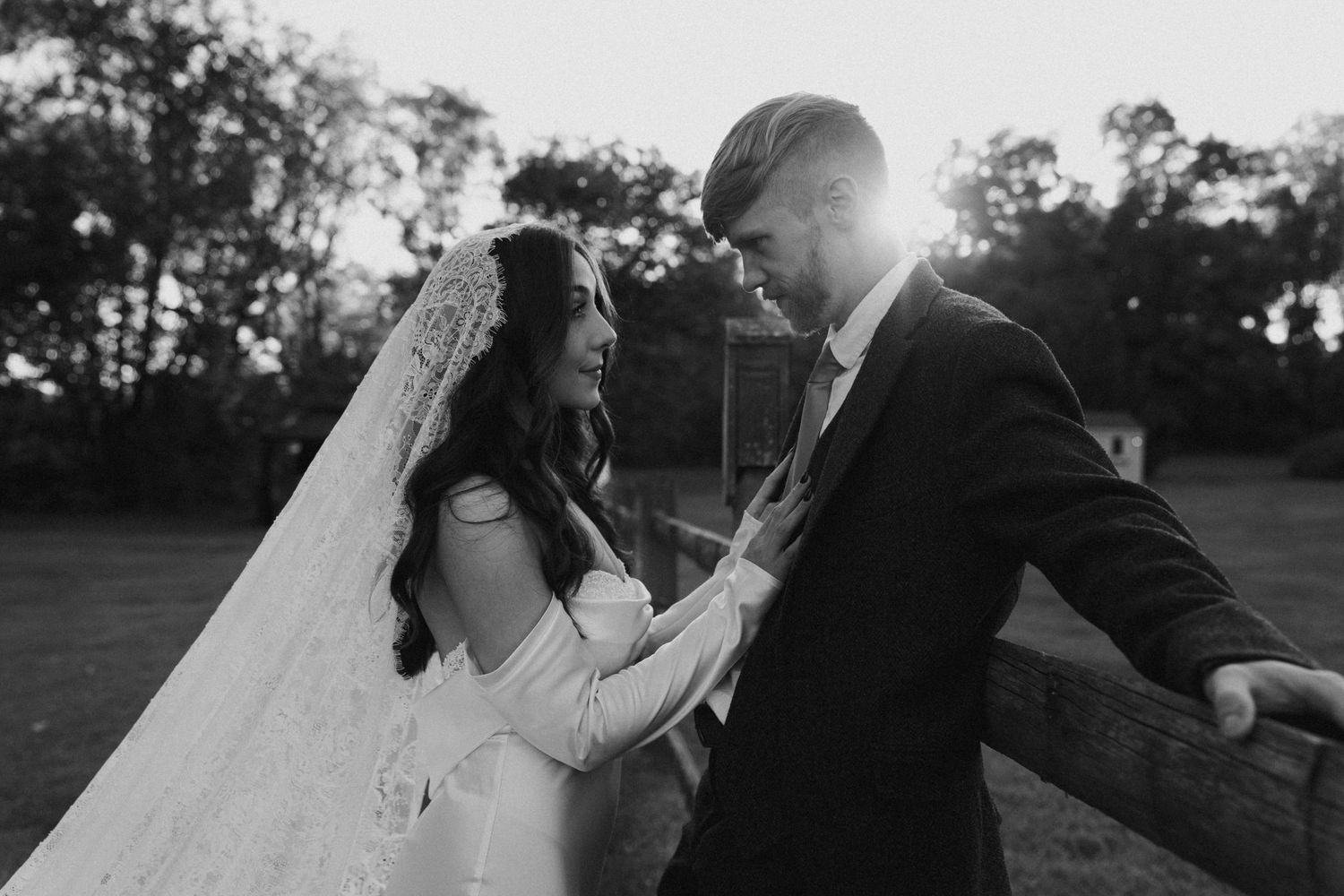 Black and white photo of newlyweds sharing intimate moment in sunlit garden.