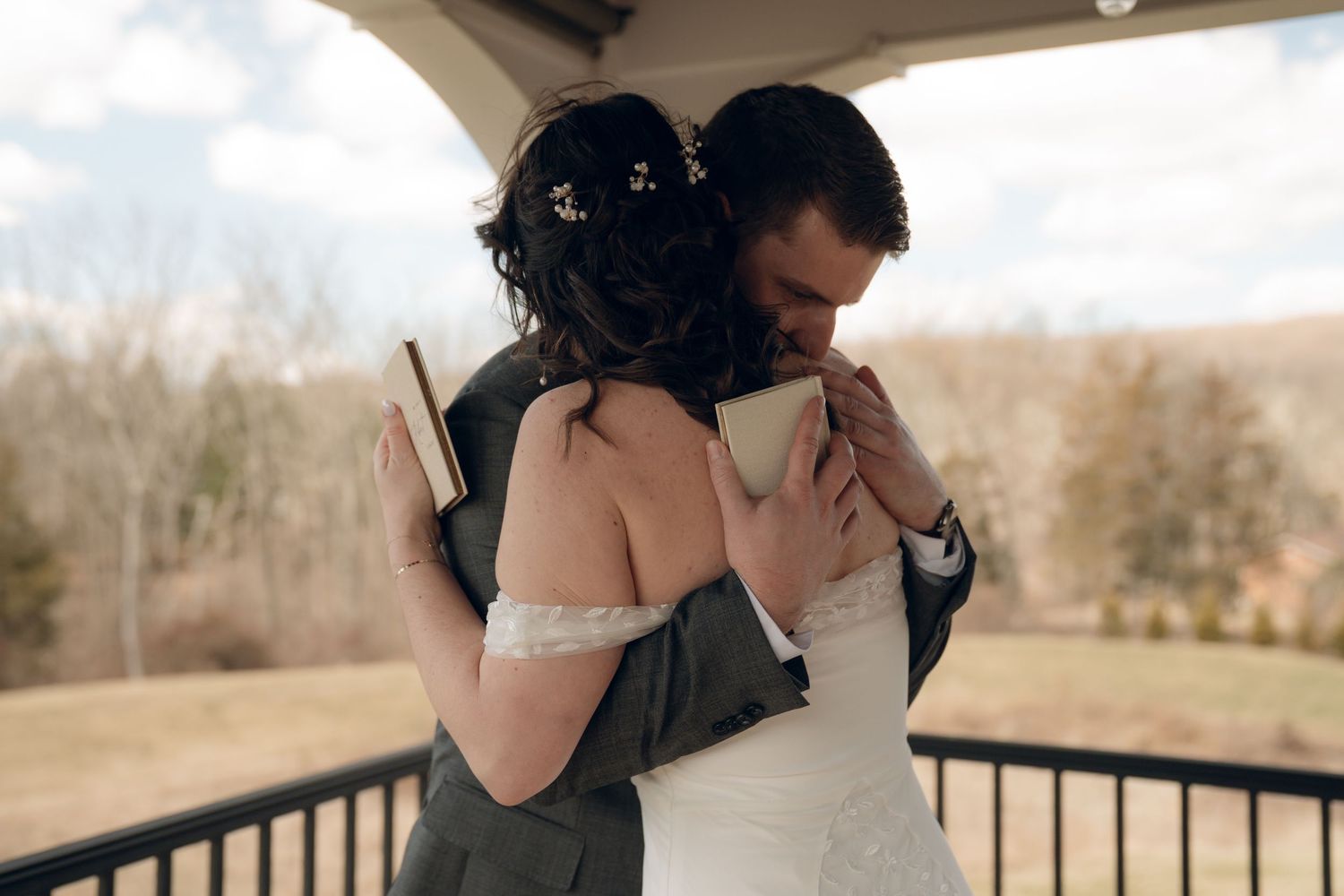 Beautiful intimate moment between newlyweds sharing an embrace on outdoor balcony during rustic wedding ceremony.