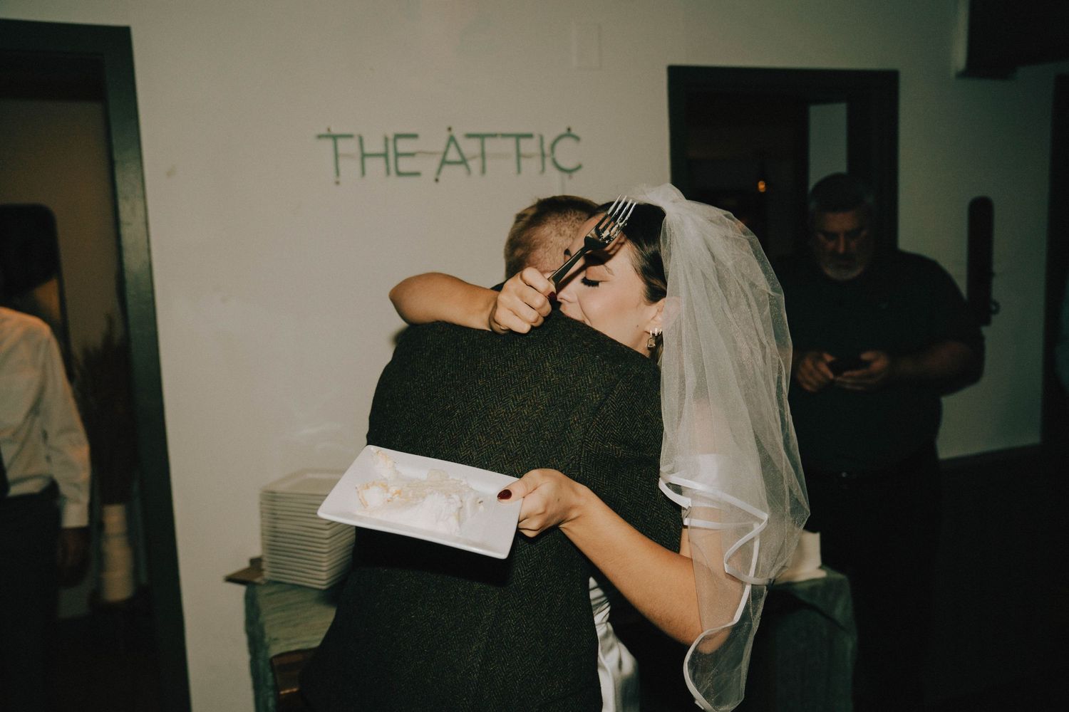 Wedding couple embracing in a dimly lit venue with 'The Attic' written on the wall.
