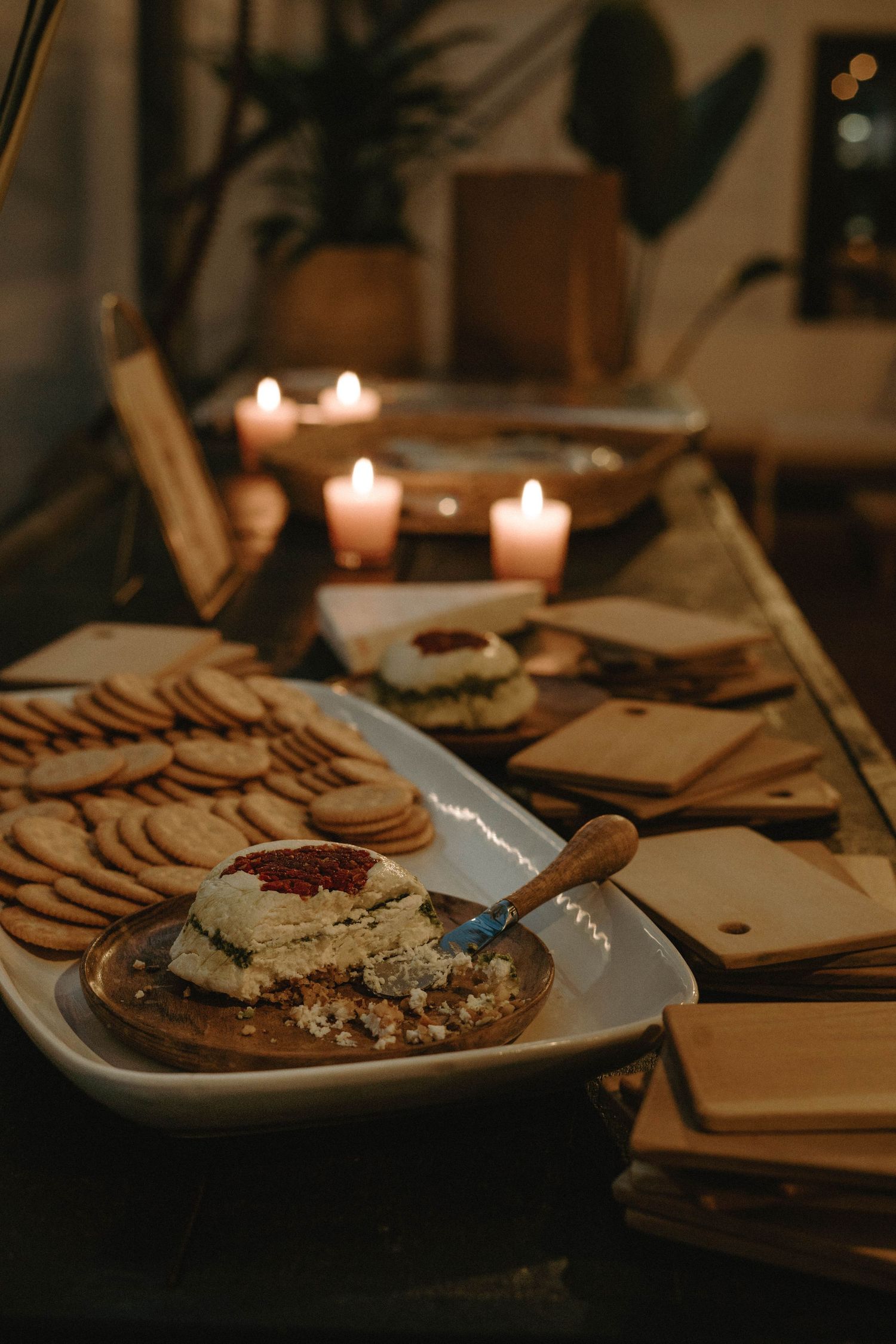 Moody candlelit table setting with appetizers and crackers arranged on serving platters.