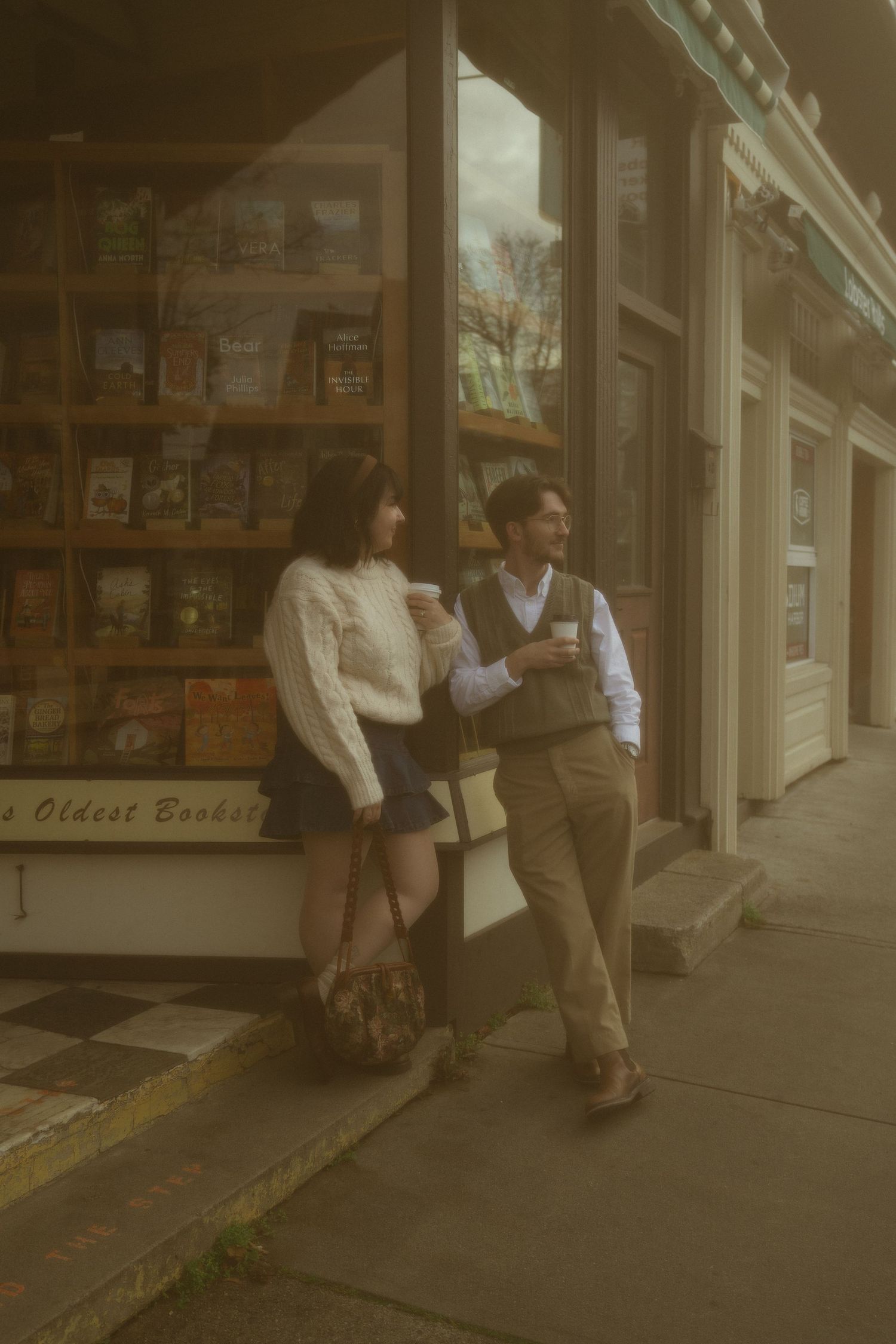 Couple sharing coffee outside a charming bookstore, woman in white blouse and mini skirt, man in vest and khakis.
