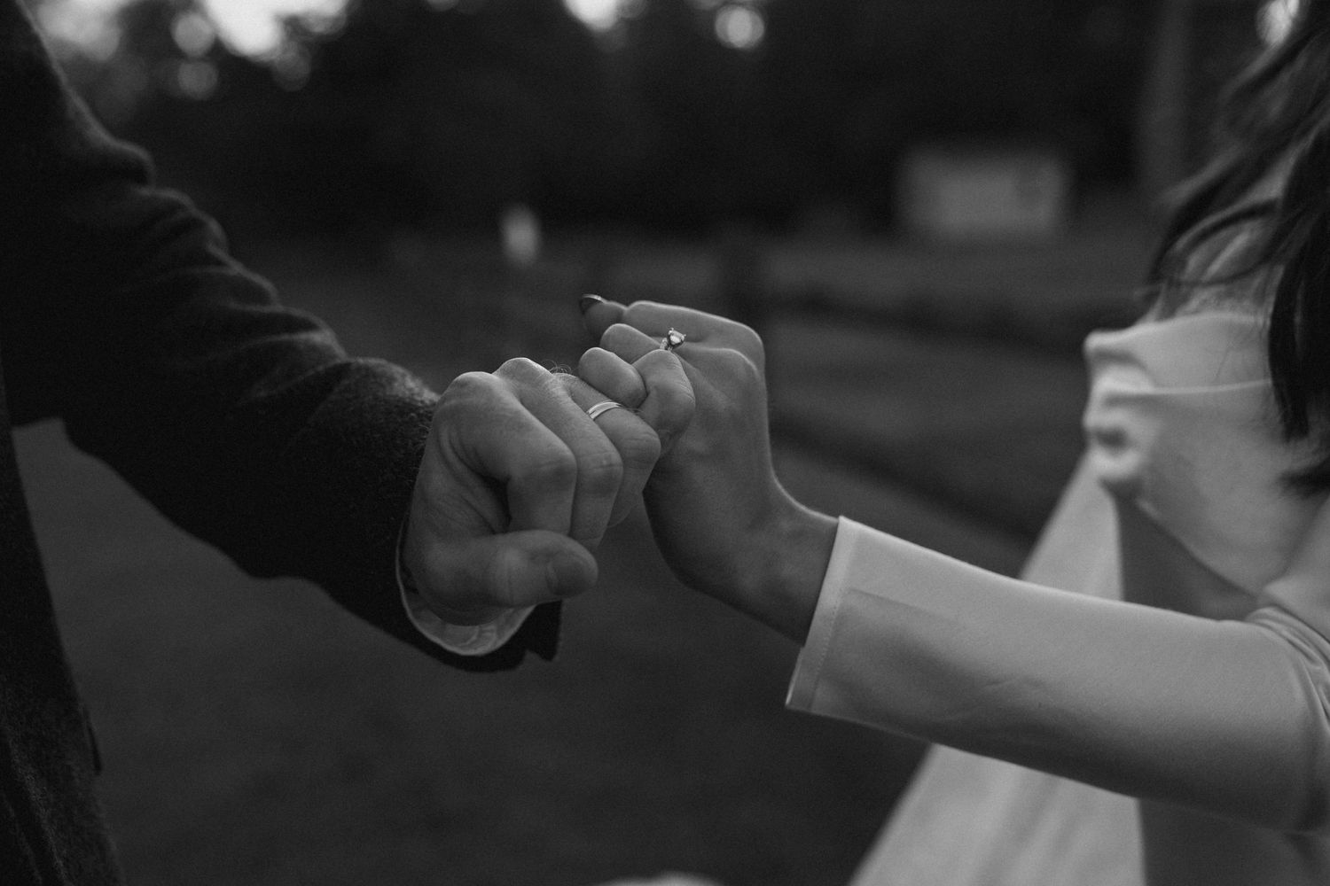 A black and white close-up photograph of two hands making a pinky promise gesture against a blurred background.