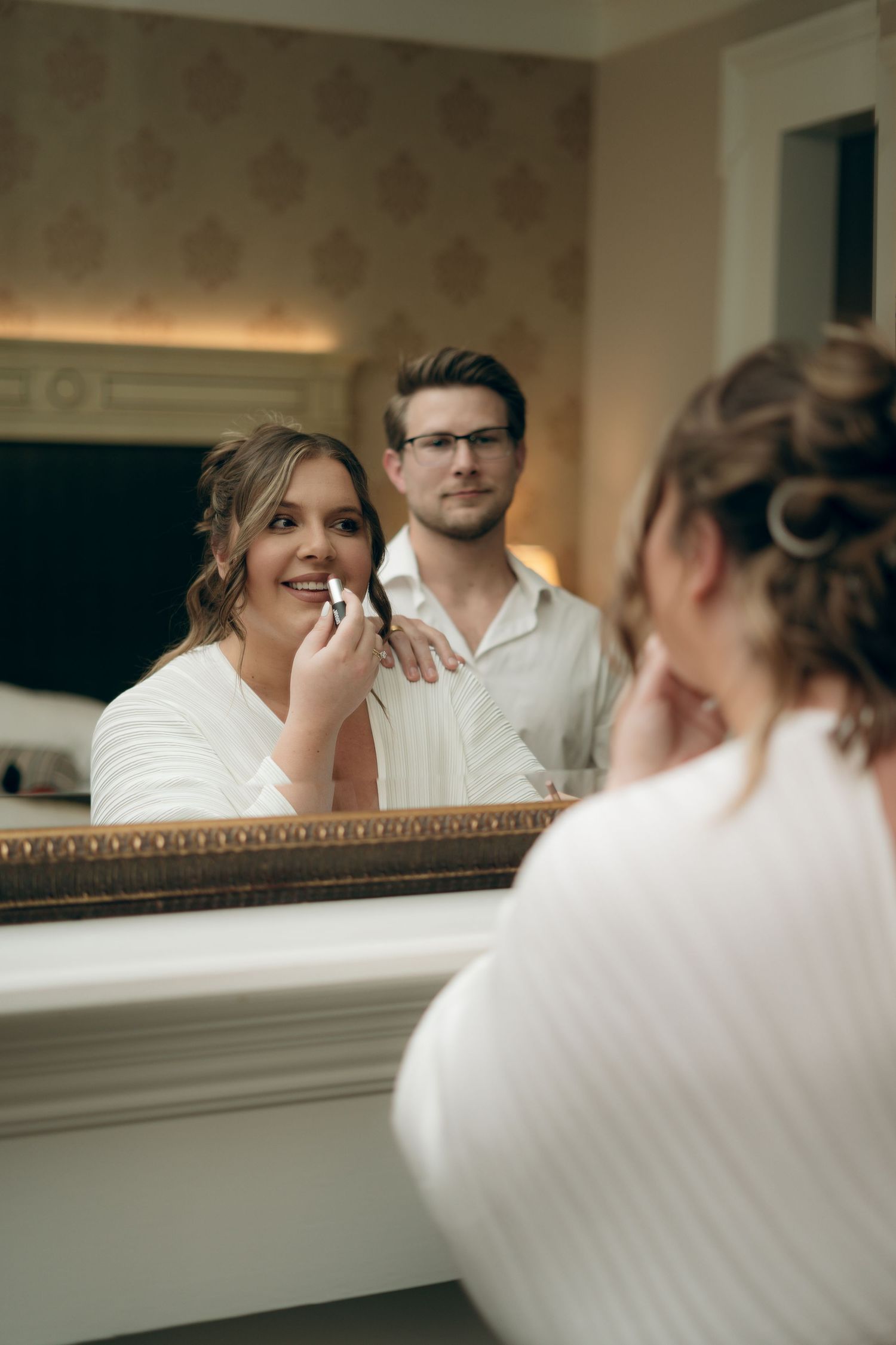 A couple gets ready in front of an ornate mirror during wedding preparations.