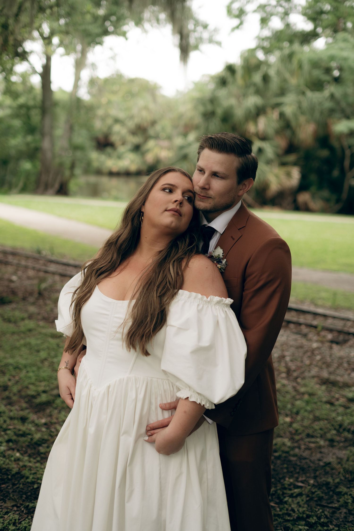 Couple shares an intimate romantic moment on grassy path in outdoor park setting.