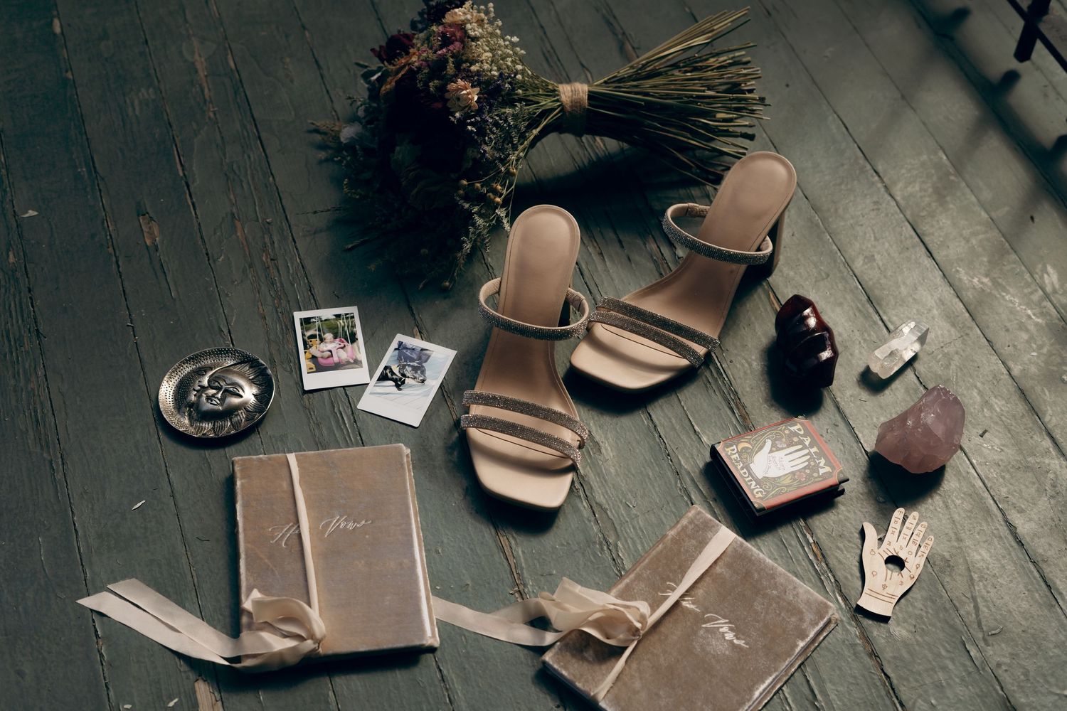 Vintage styled flatlay with sandals, books, photographs and dried flowers on a dark wooden floor.