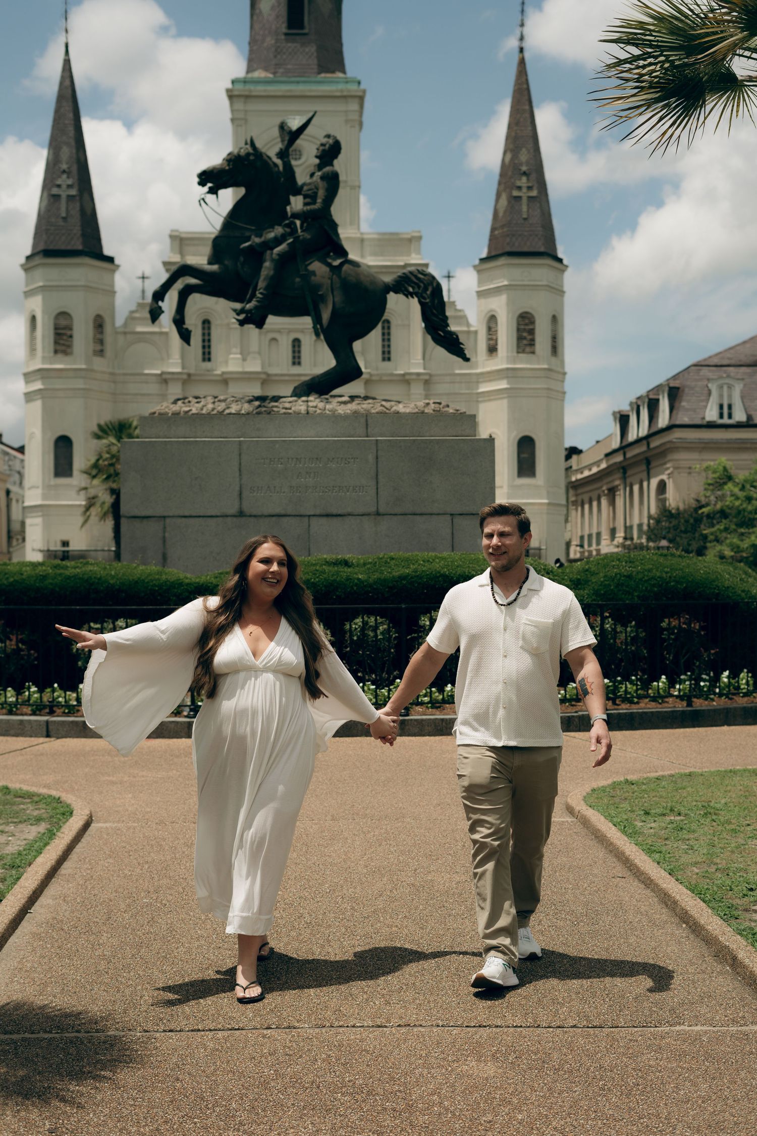 Two figures in white clothing walk together in front of St. Louis Cathedral in Jackson Square, New Orleans.