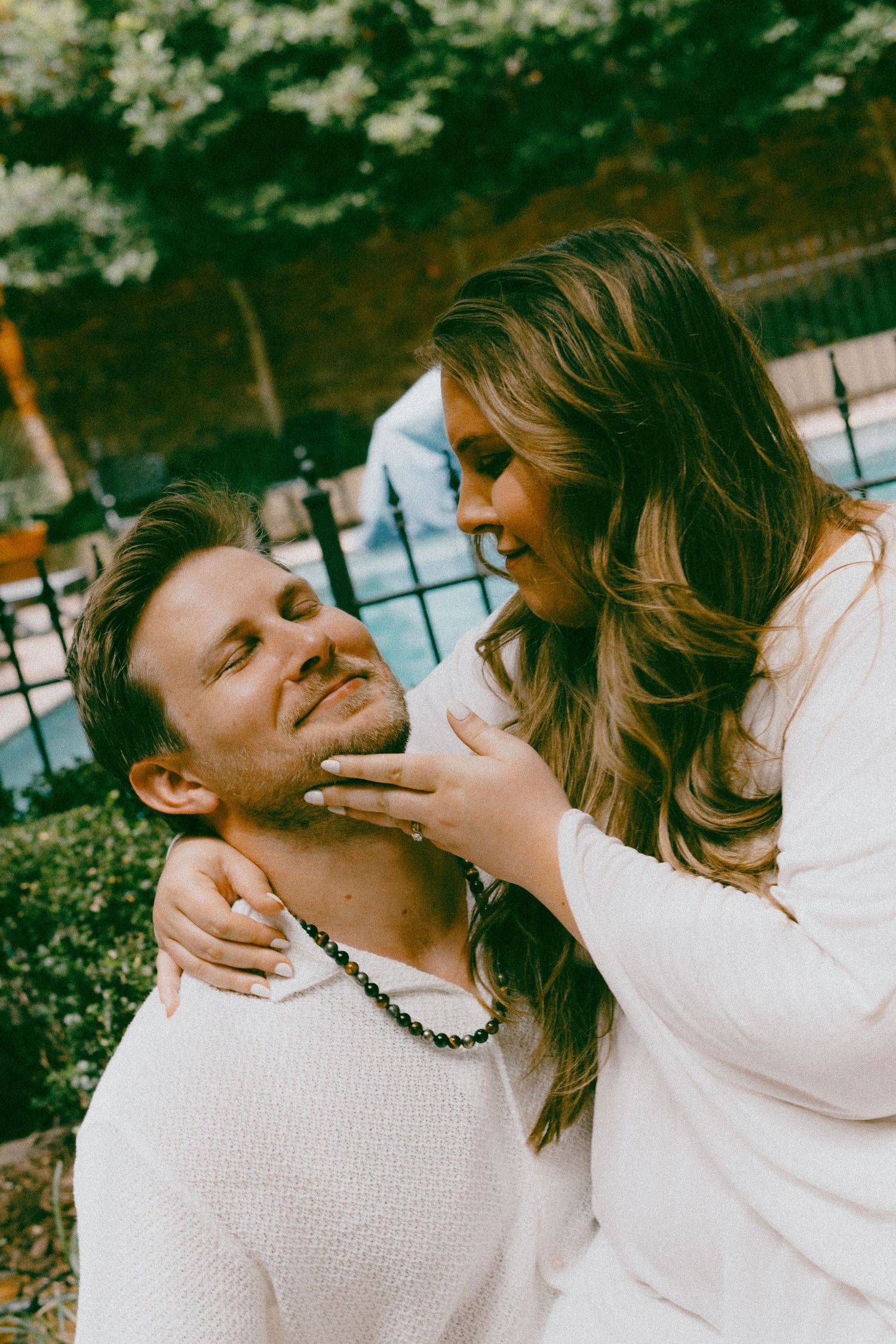 A playful couple in white outfits share an affectionate moment outdoors.