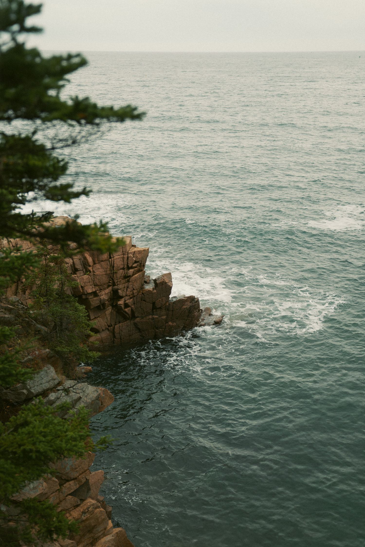 Rocky coastal cliffs meet the deep blue ocean waters with white waves crashing against the rugged shoreline.