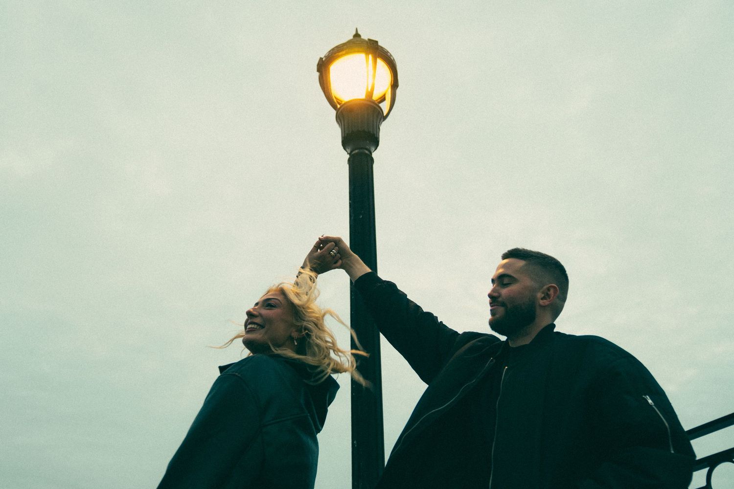 Two people stand beneath a glowing vintage street lamp at dusk. Couple in Bar Harbor Maine