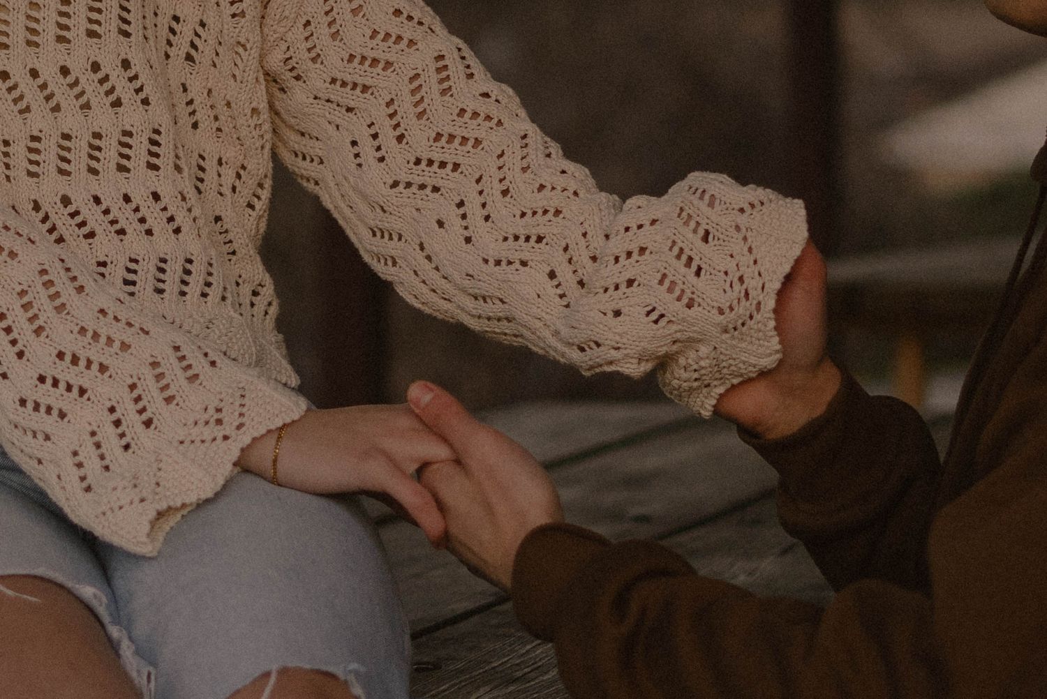 Close up of hands wearing white knit sweater and brown jacket.