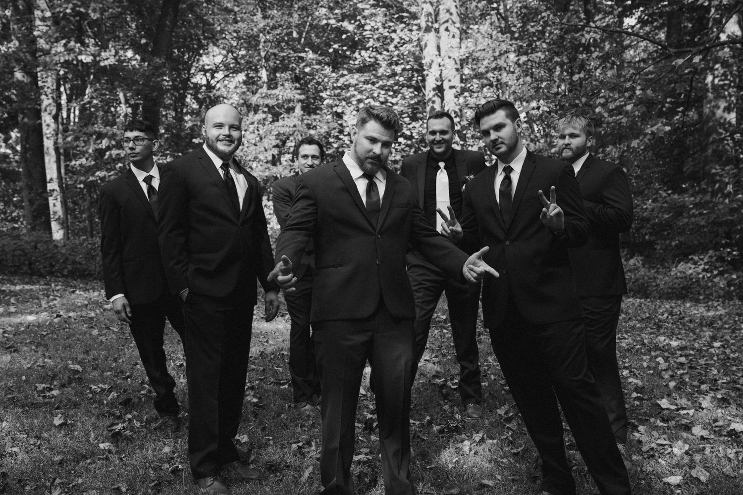 Black and white photo of groomsmen in suits posing in a wooded setting.